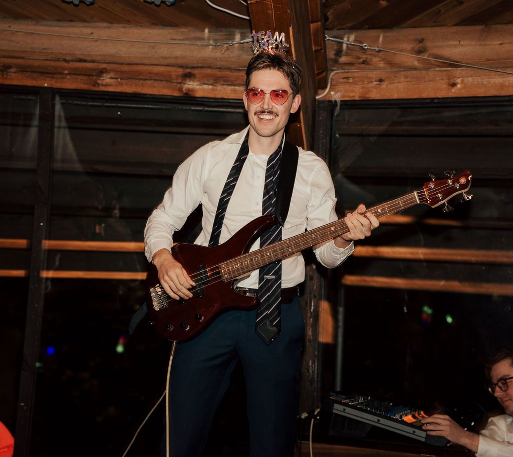 Musician plays bass guitar during a performance in a rustic wooden venue with warm lighting.