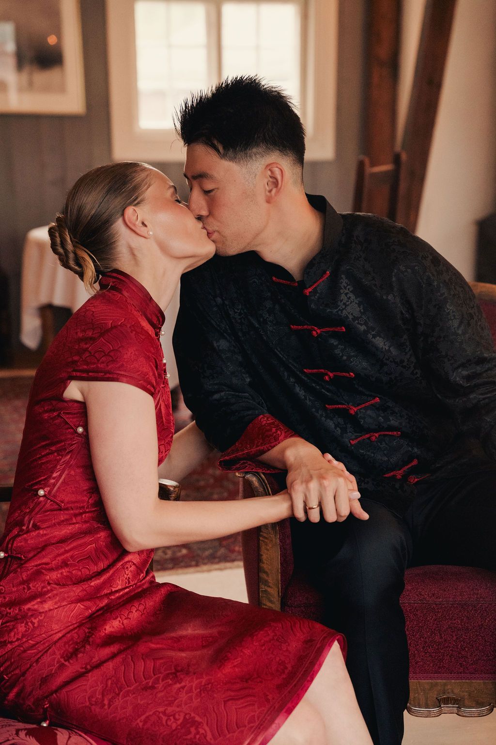 A couple in traditional Chinese attire share an intimate moment, with her in red qipao and him in black mandarin collar suit.