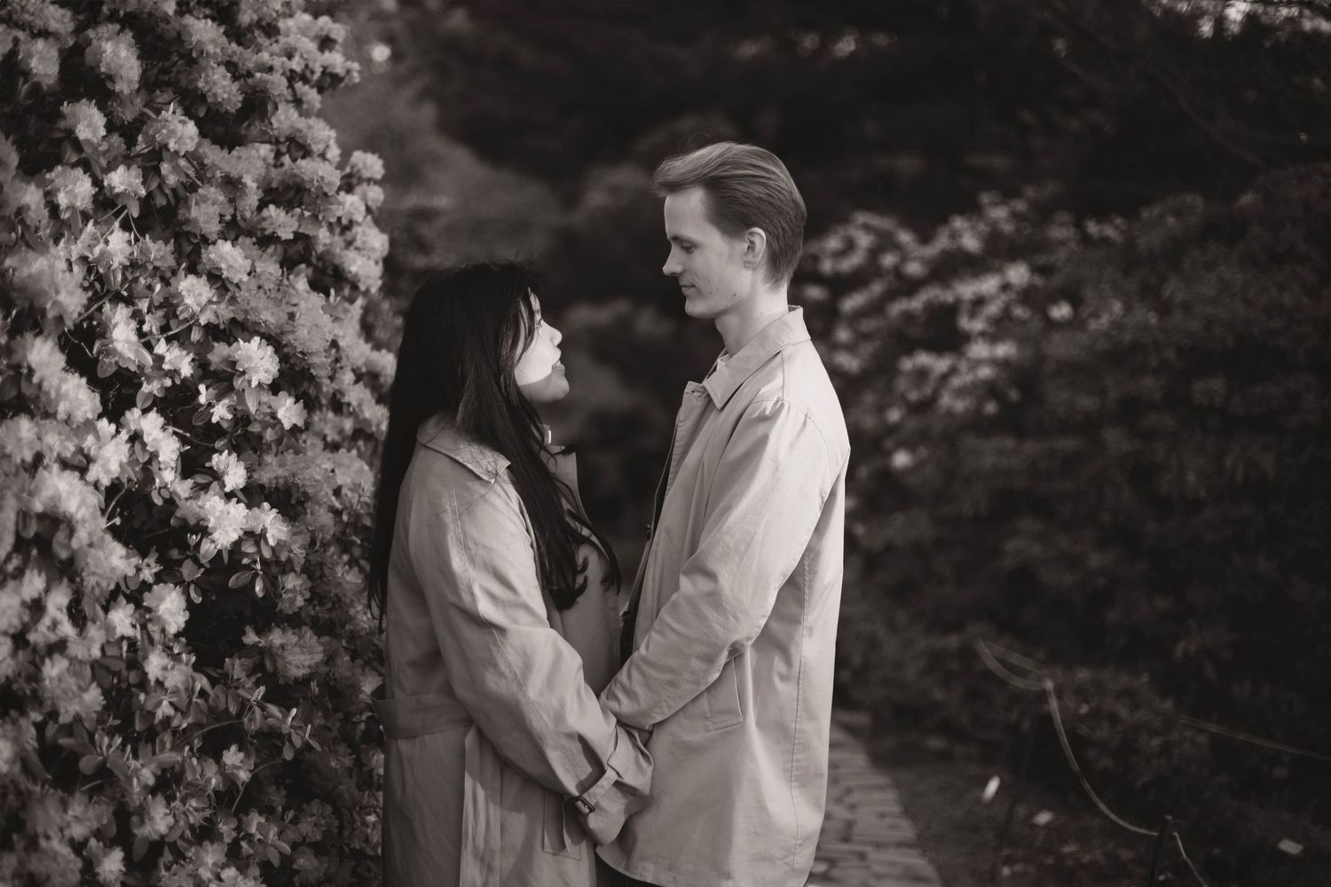 A couple shares a tender moment together in a garden filled with blooming white flowers and lush greenery.