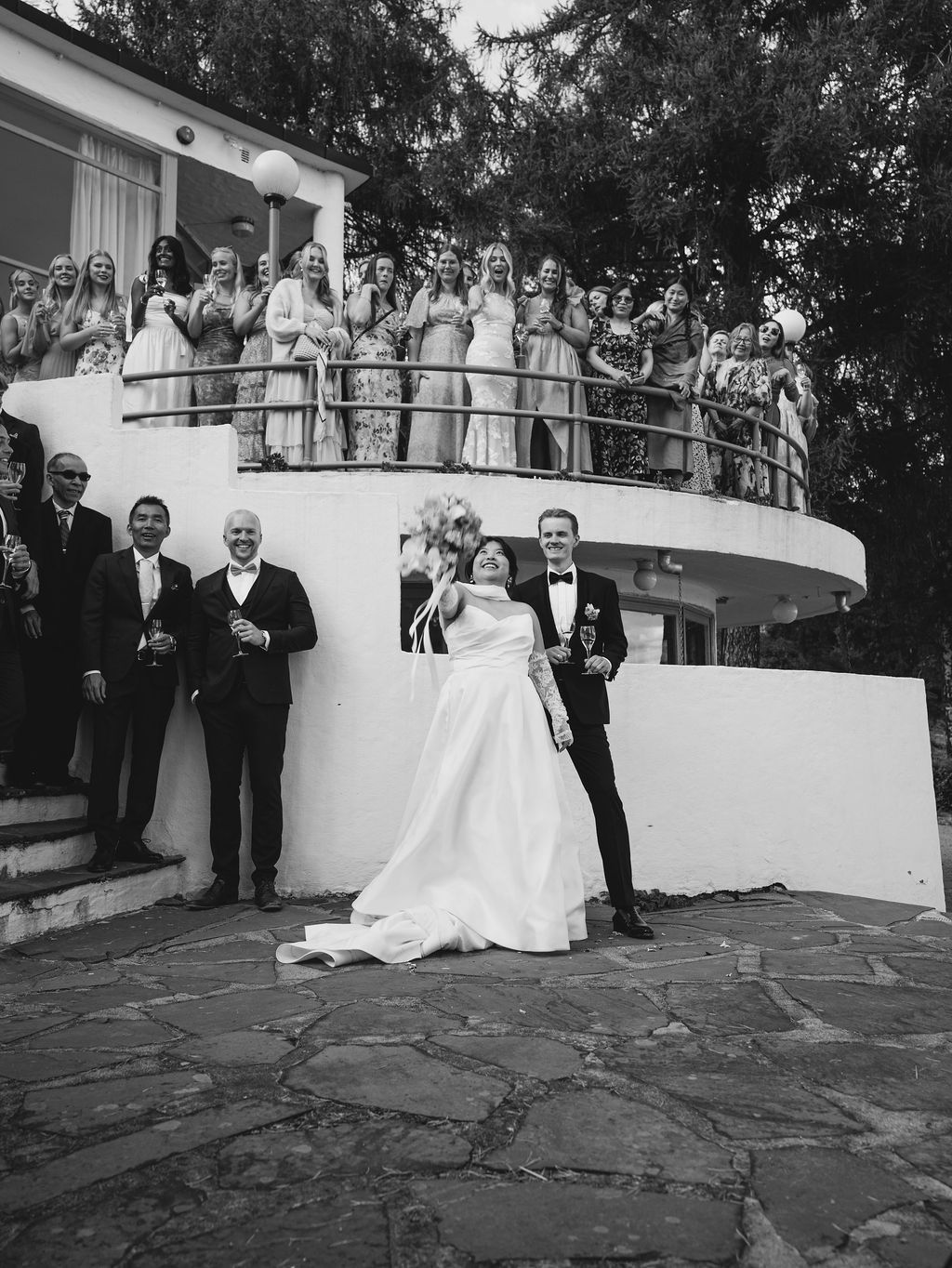 A wedding couple descends a curved white staircase surrounded by guests during their outdoor ceremony.