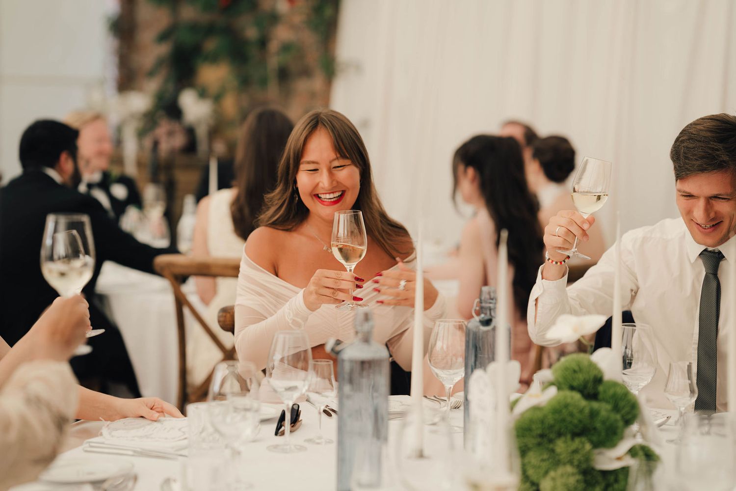 Guests laughing and toasting with wine glasses at an elegant wedding reception dinner.