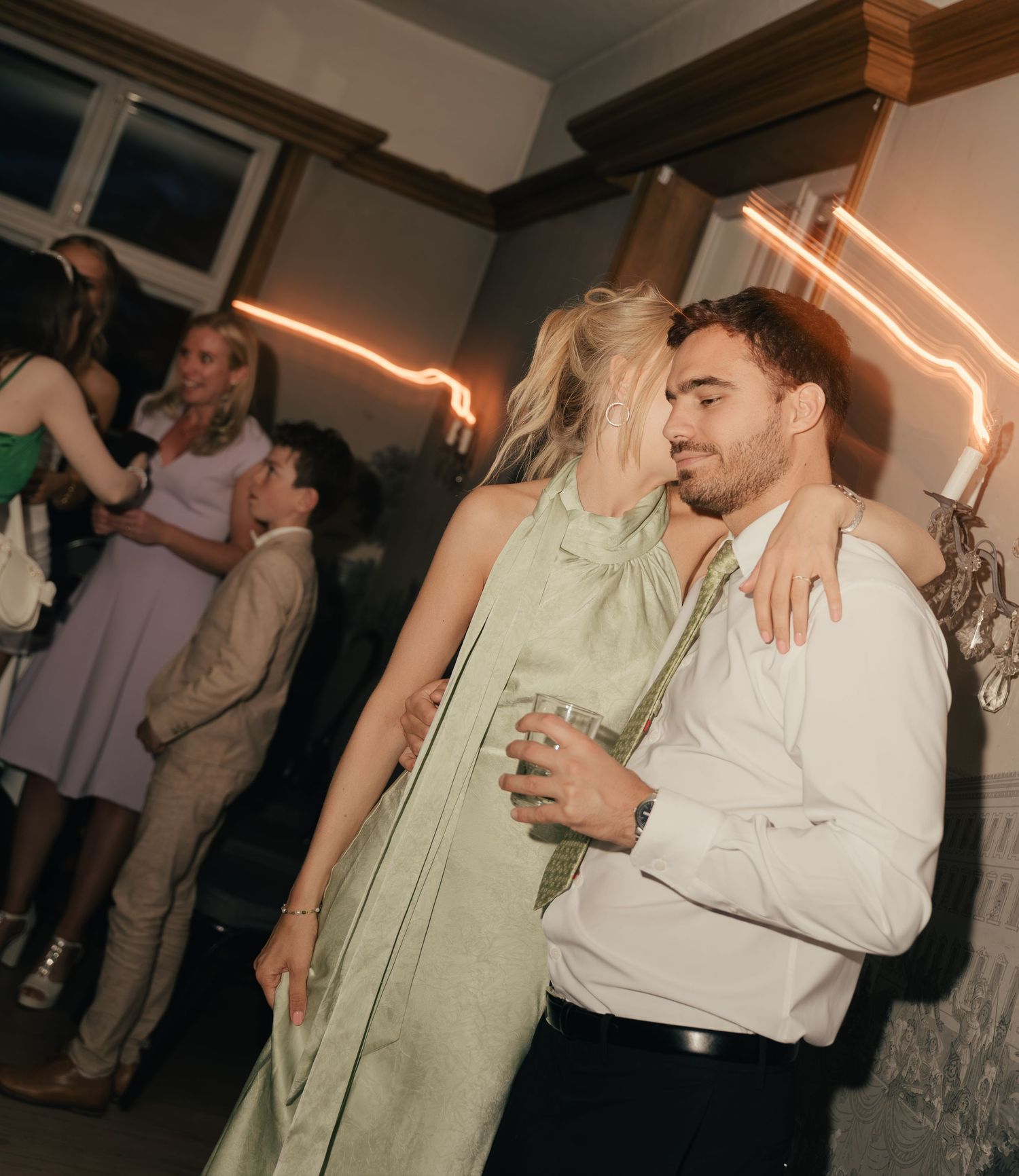 Couple in formal attire dance closely together at indoor wedding reception party.