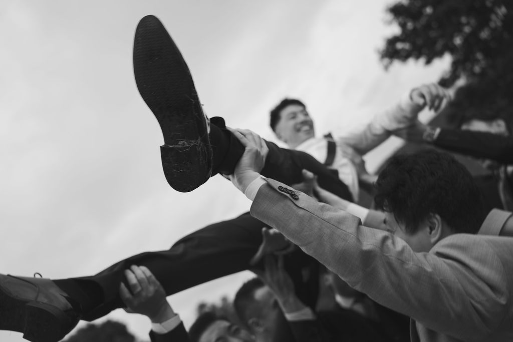 A black and white panoramic sequence shows people raising their arms in celebration at an outdoor event.