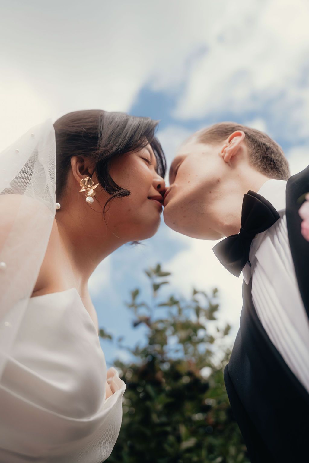 A romantic sequence of wedding photos showing a couple kissing under a cloudy sky with greenery in the background.