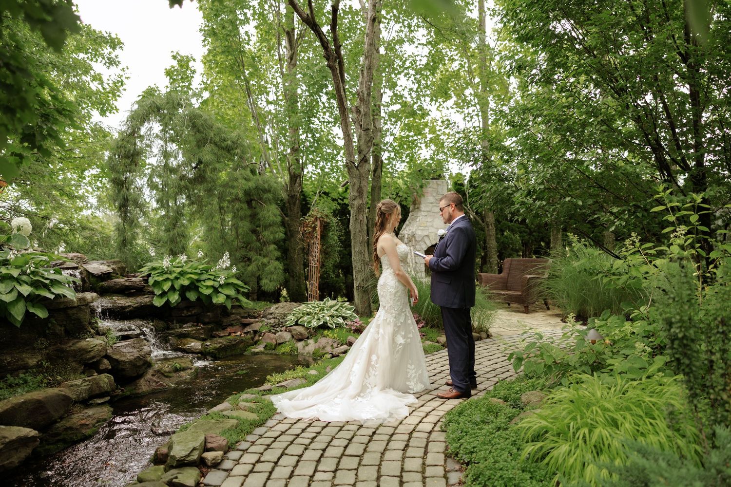 Bride and groom share a romantic moment on a brick garden path surrounded by lush greenery and a waterfall.
