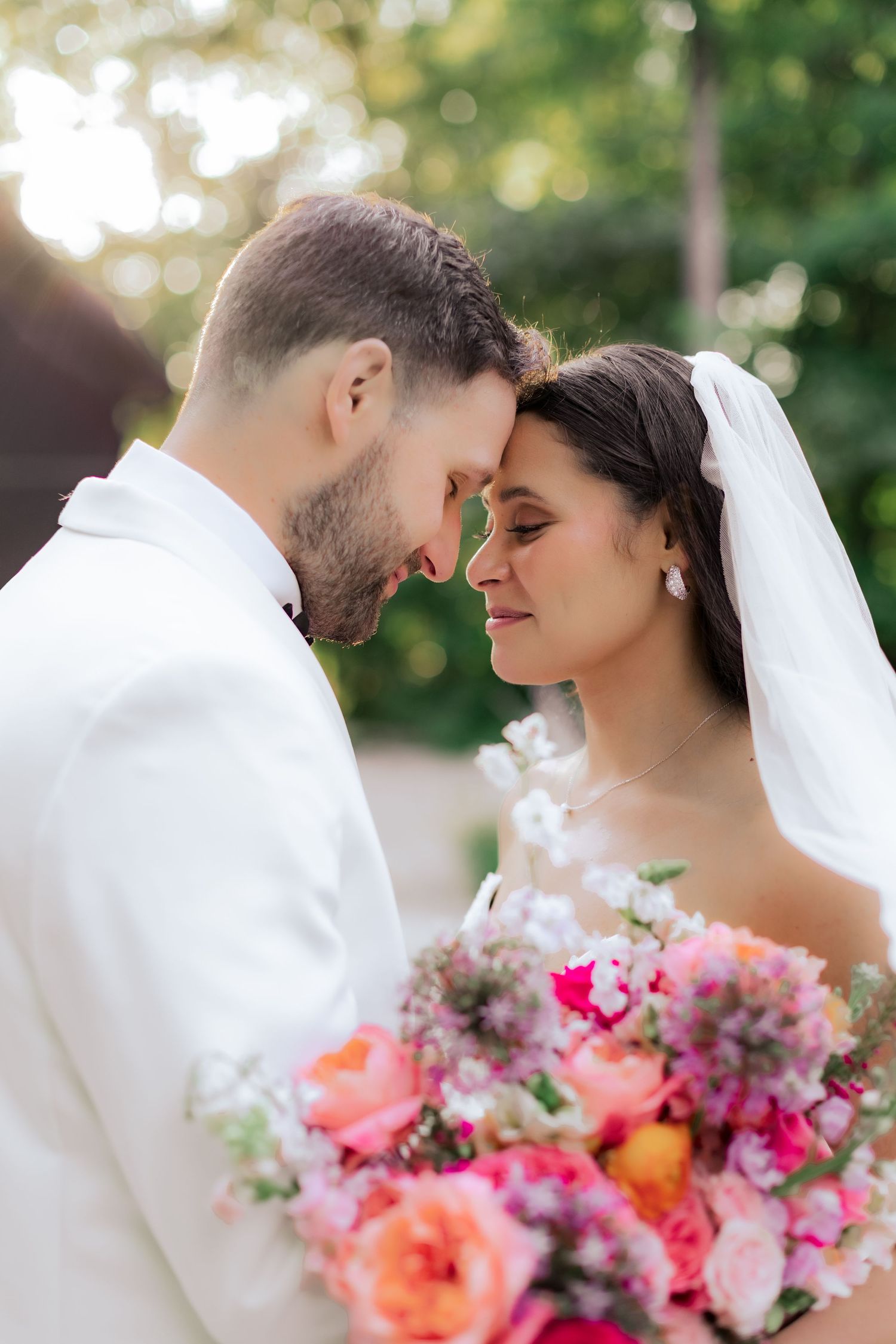 Romantic wedding moment captured outdoors with stunning coral and pink bouquet against soft bokeh background.