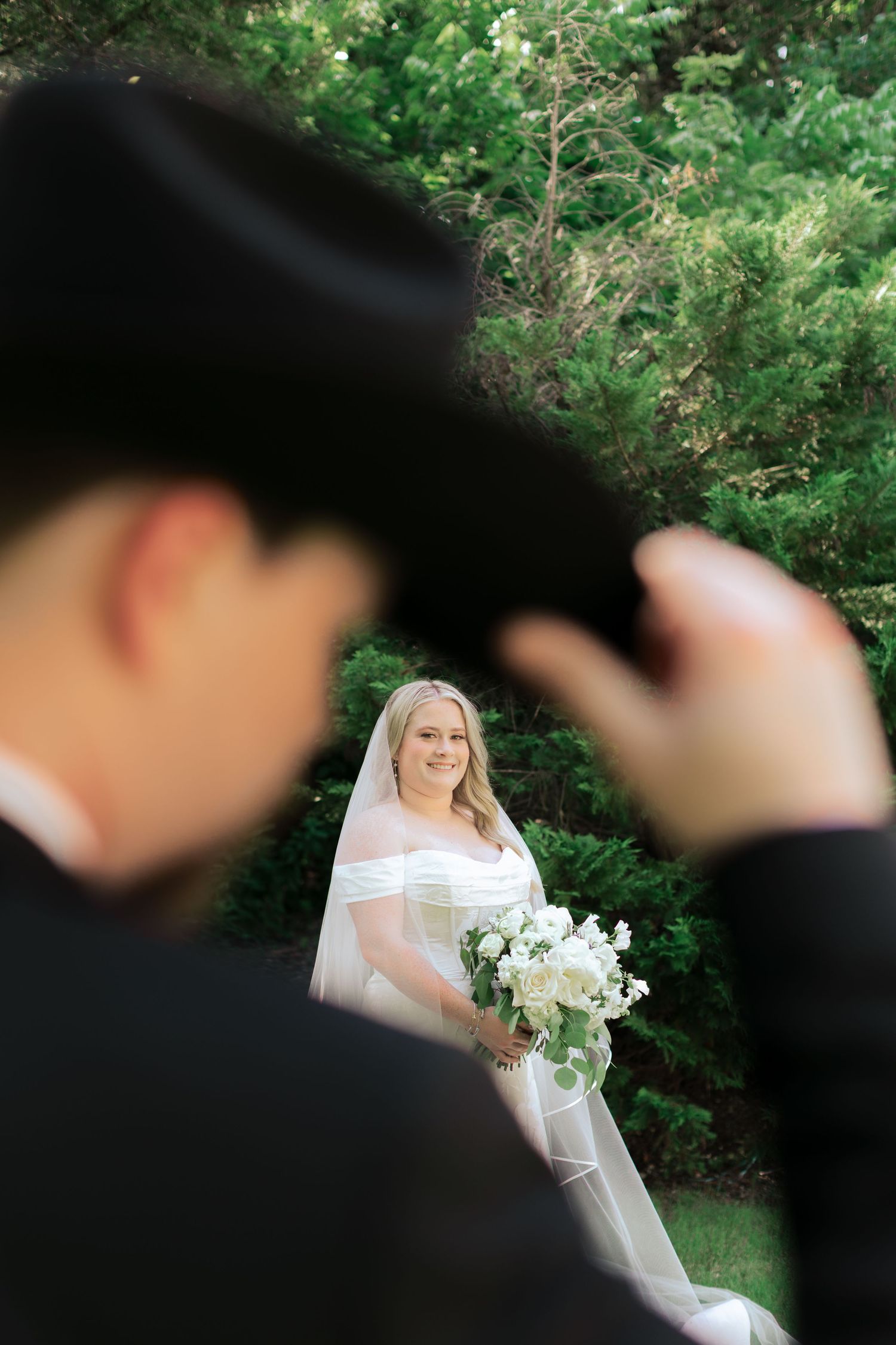 Bride in white dress holds bouquet while posing in garden setting with dramatic lighting.
