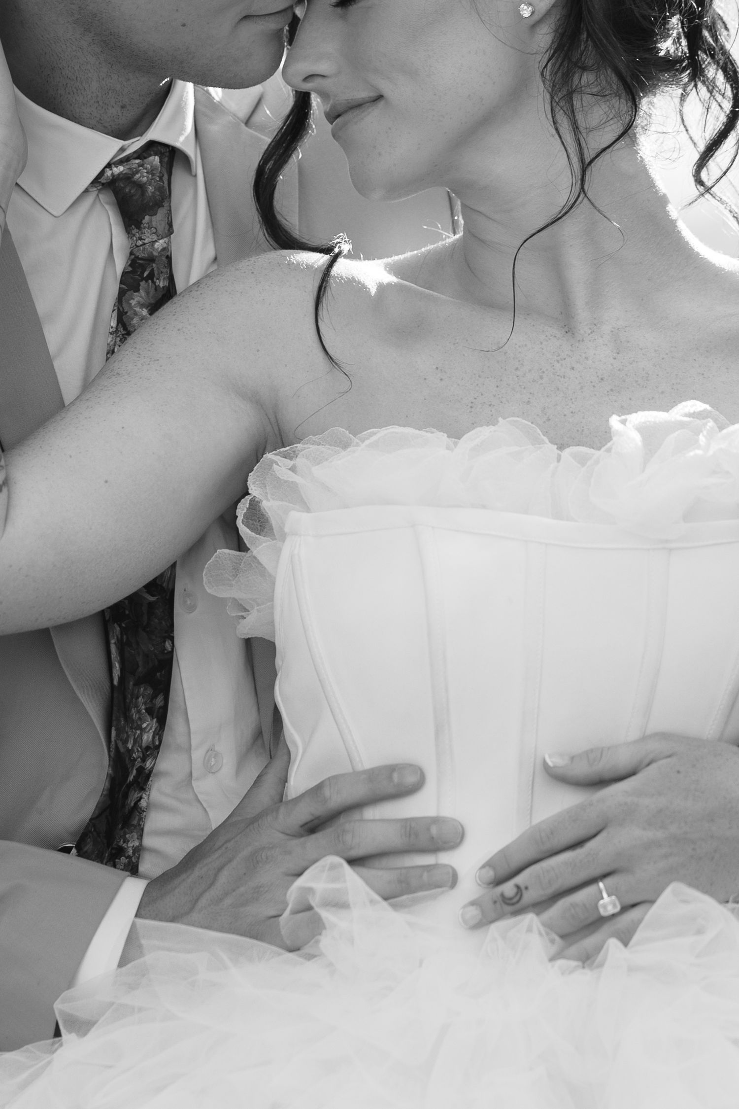 Black and white photo of a bride and groom in an intimate moment, her diamond ring visible on his hand at her waist.