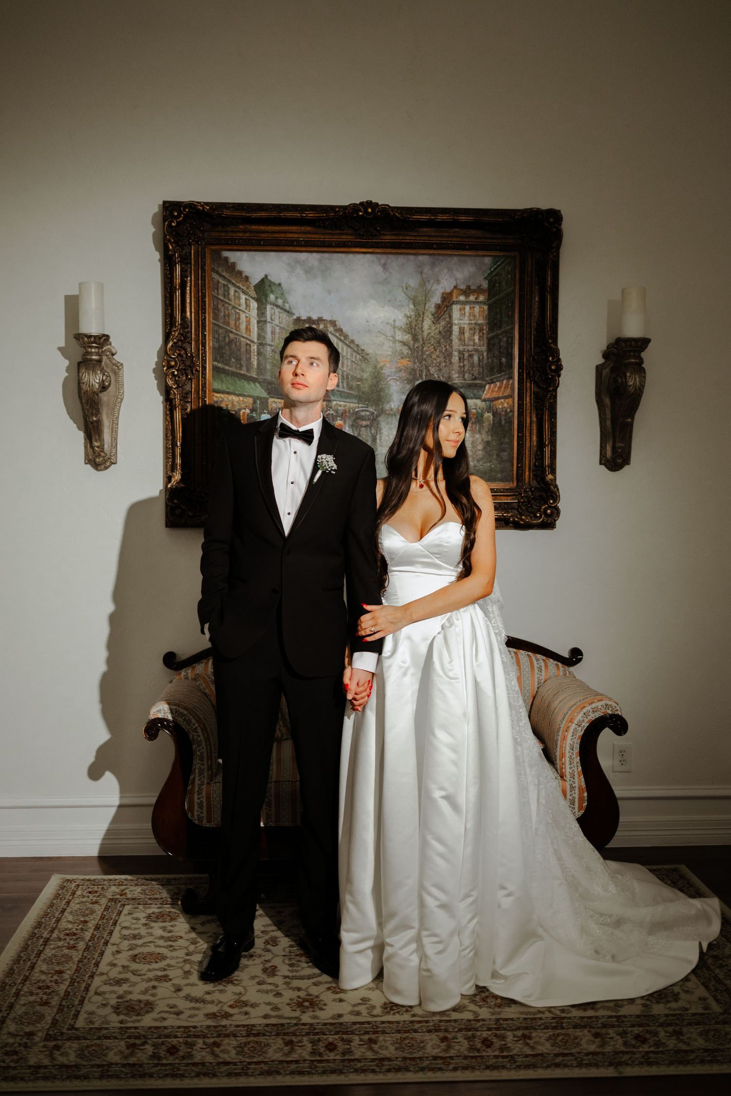 A formal couple poses together in an elegant room with ornate decor and a patterned rug.