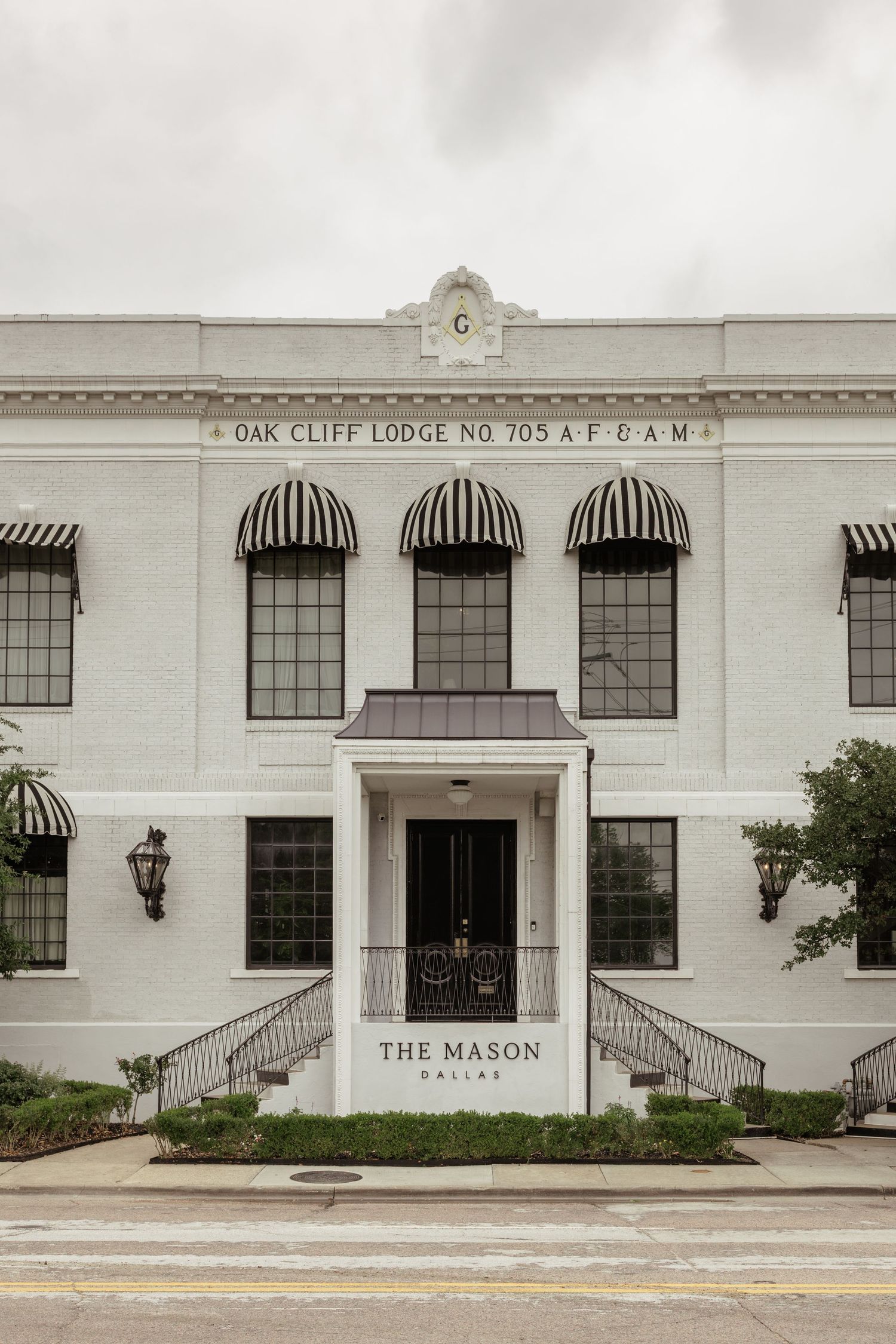 The Mason Dallas historic white building, Oak Cliff Lodge No. 705 AF&AM, featuring black striped awnings and elegant entrance.