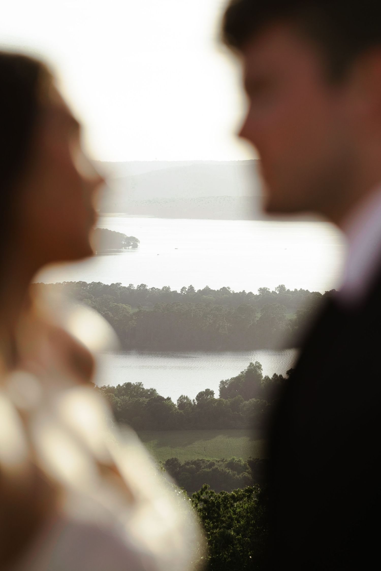 Blurred couple in foreground with scenic river and lush green landscape in soft golden light background.