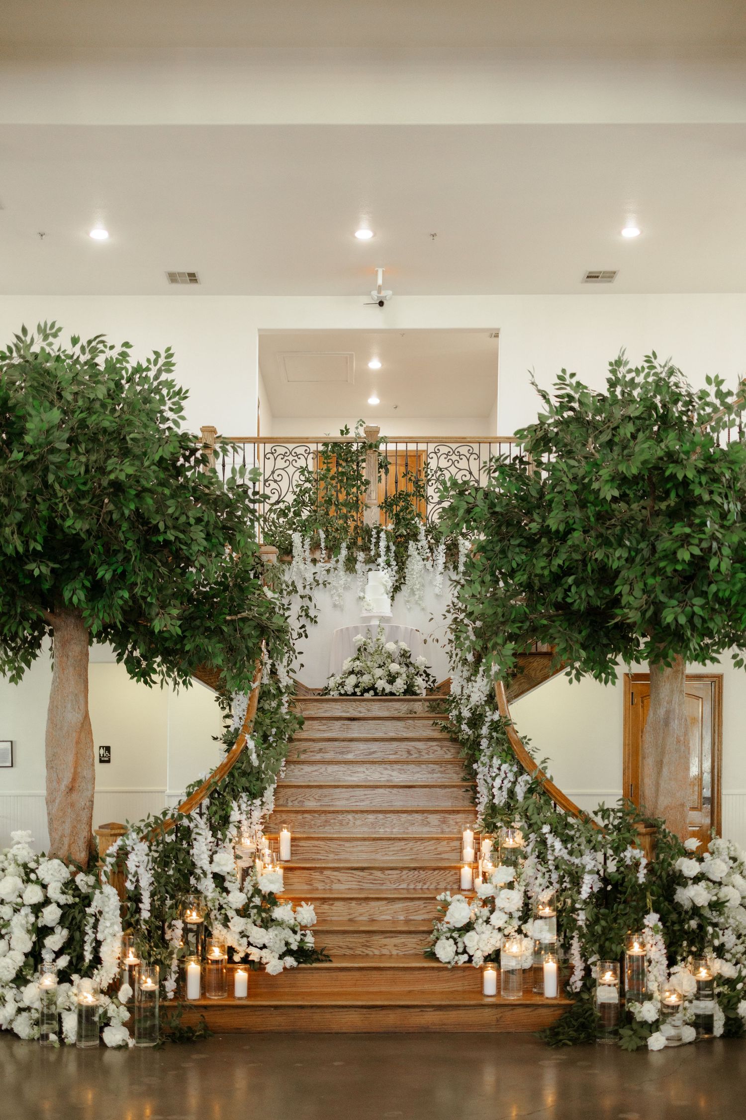 Elegant wedding staircase adorned with white flowers, greenery, and candles in a grand venue.