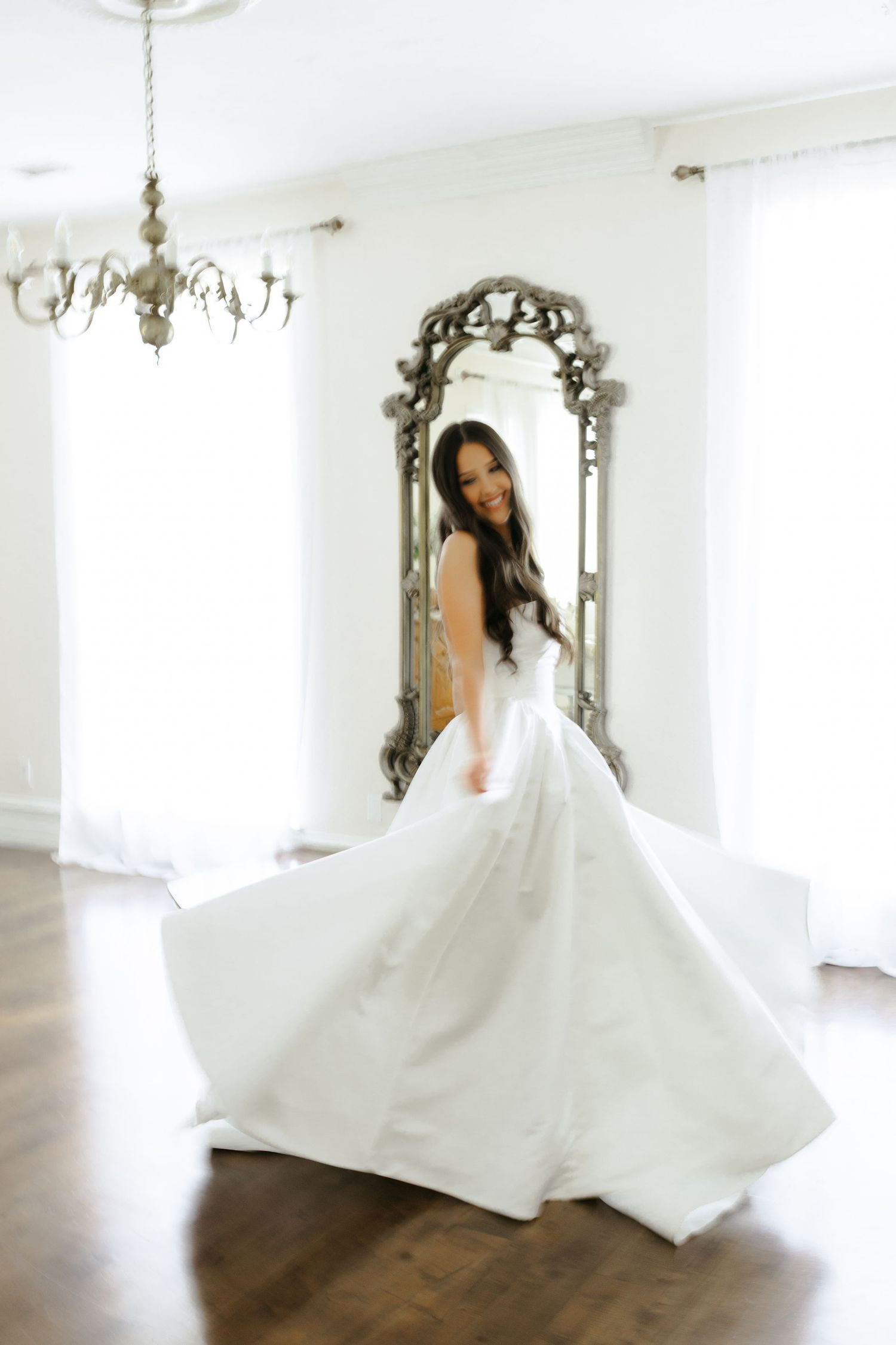 A bride in a flowing white ballgown twirls elegantly in a bright indoor space with ornate mirrors.
