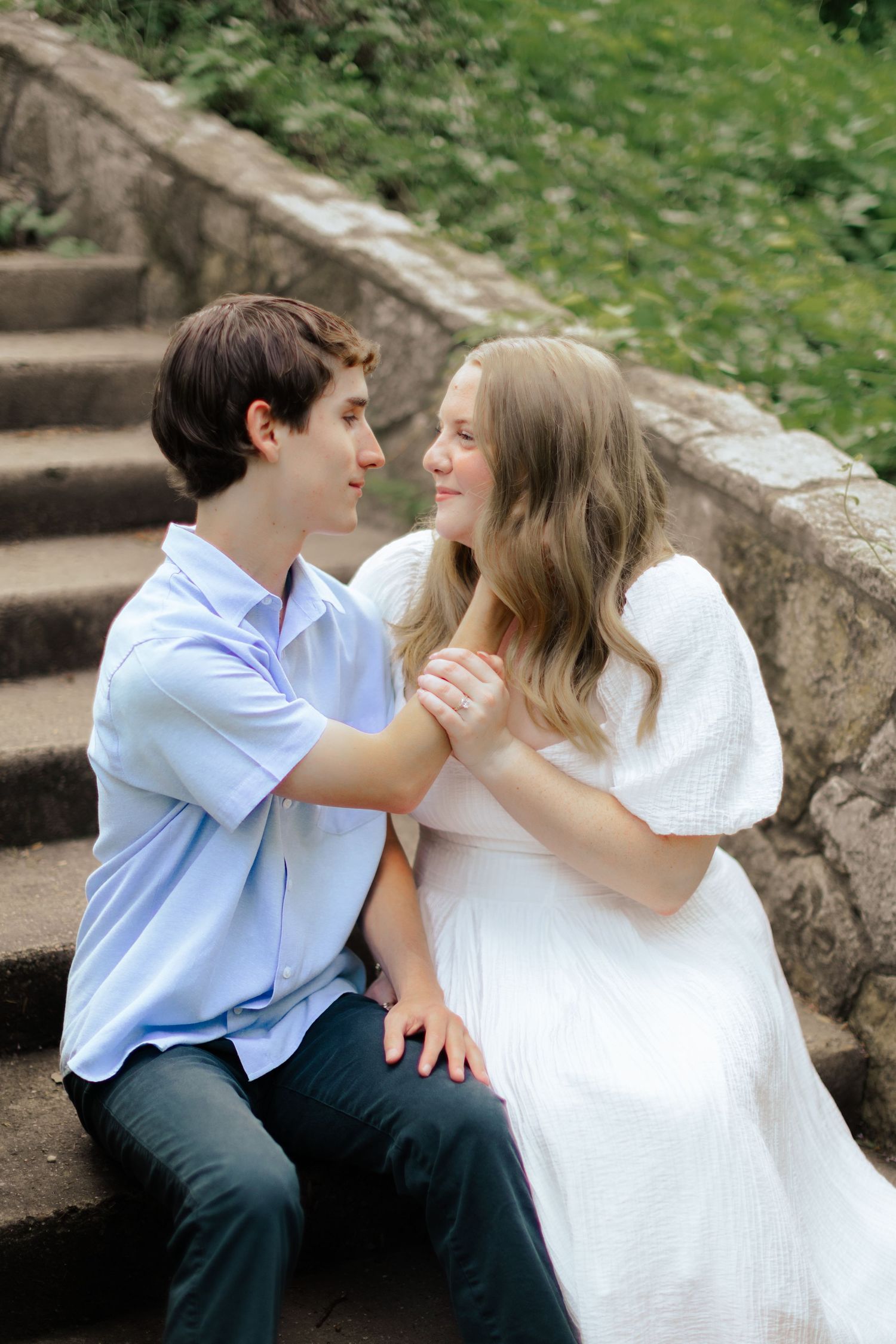 Romantic couple shares tender moment while sitting on stone steps in garden setting.