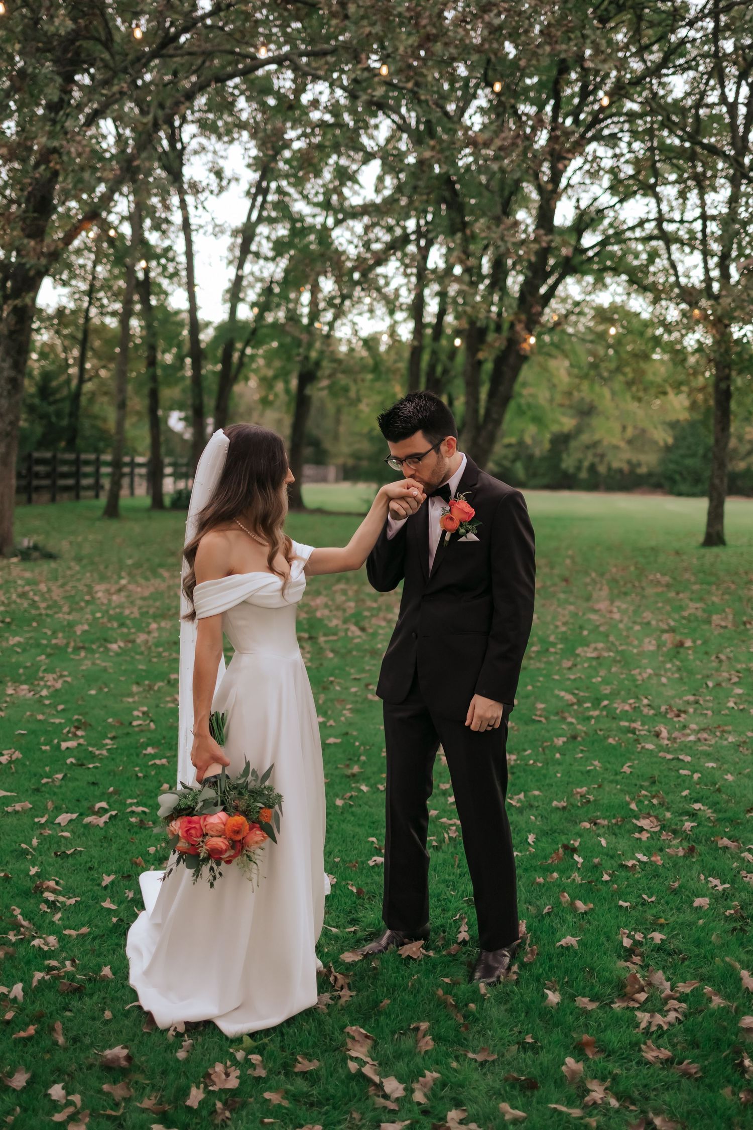 A couple shares a playful moment on a grassy lawn covered in autumn leaves during their wedding photoshoot.