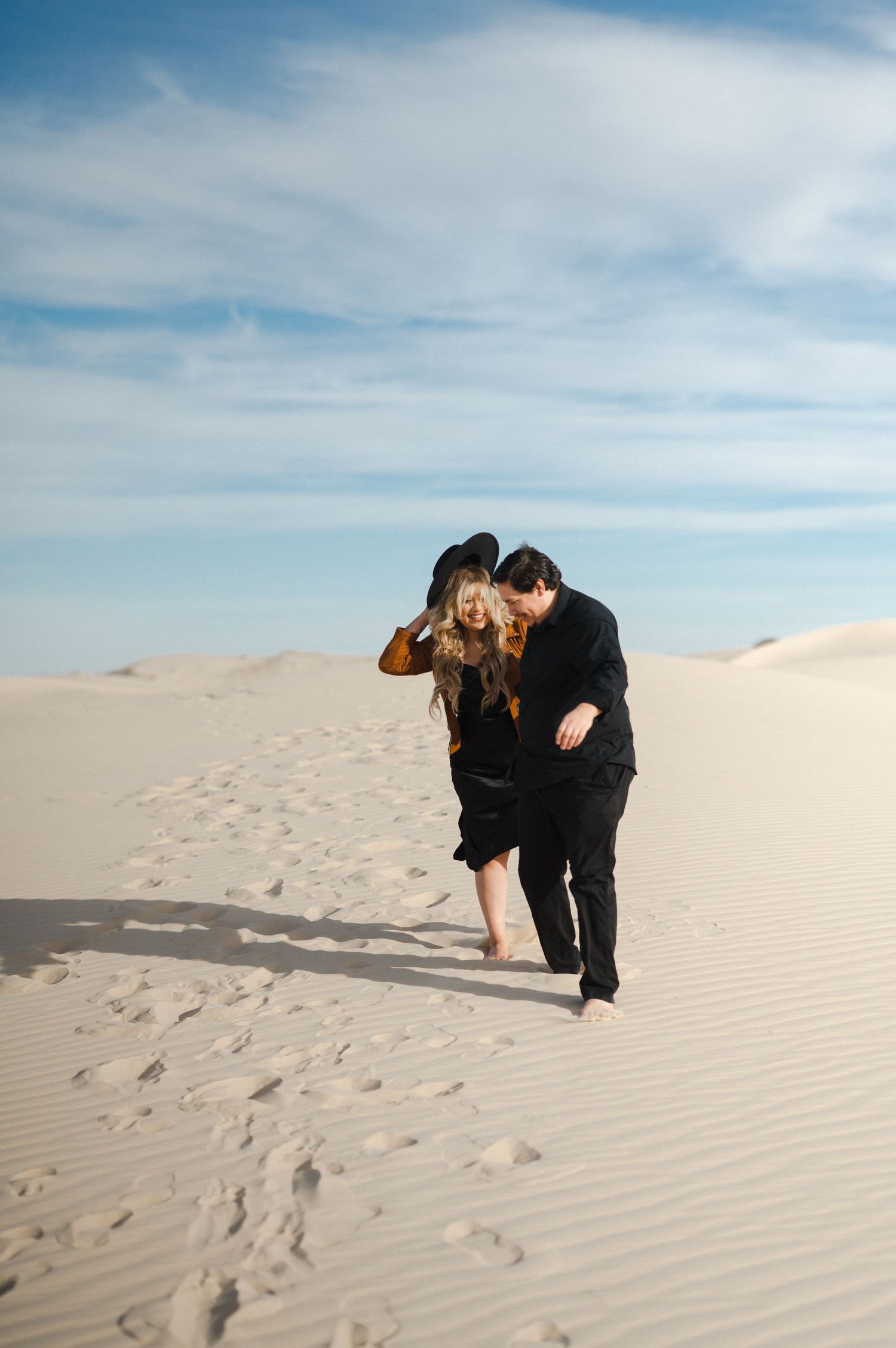 Couple walking together on pristine white sand dunes under blue sky.