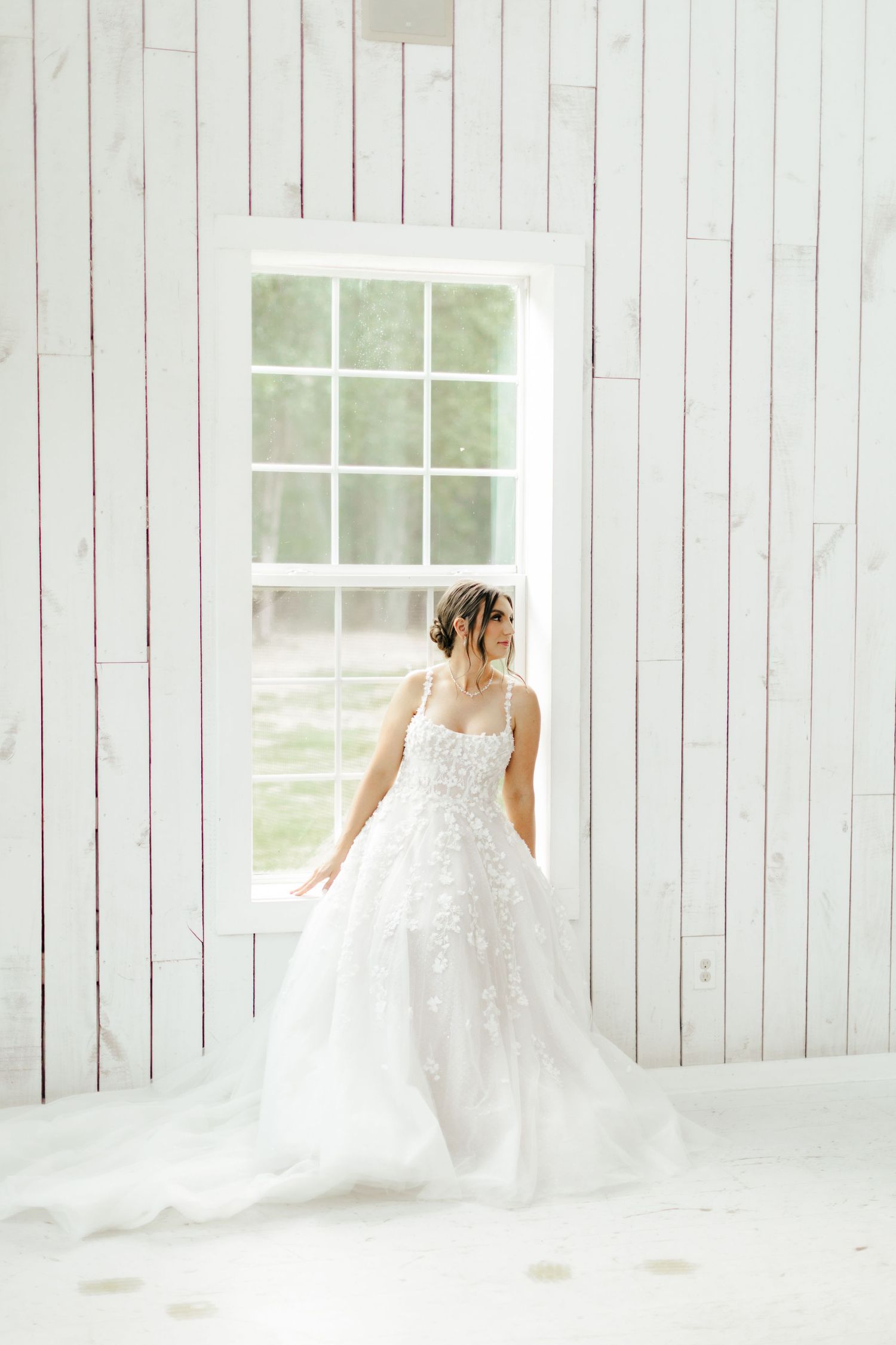 An elegant white wedding gown with lace details photographed in a bright rustic room with white walls.