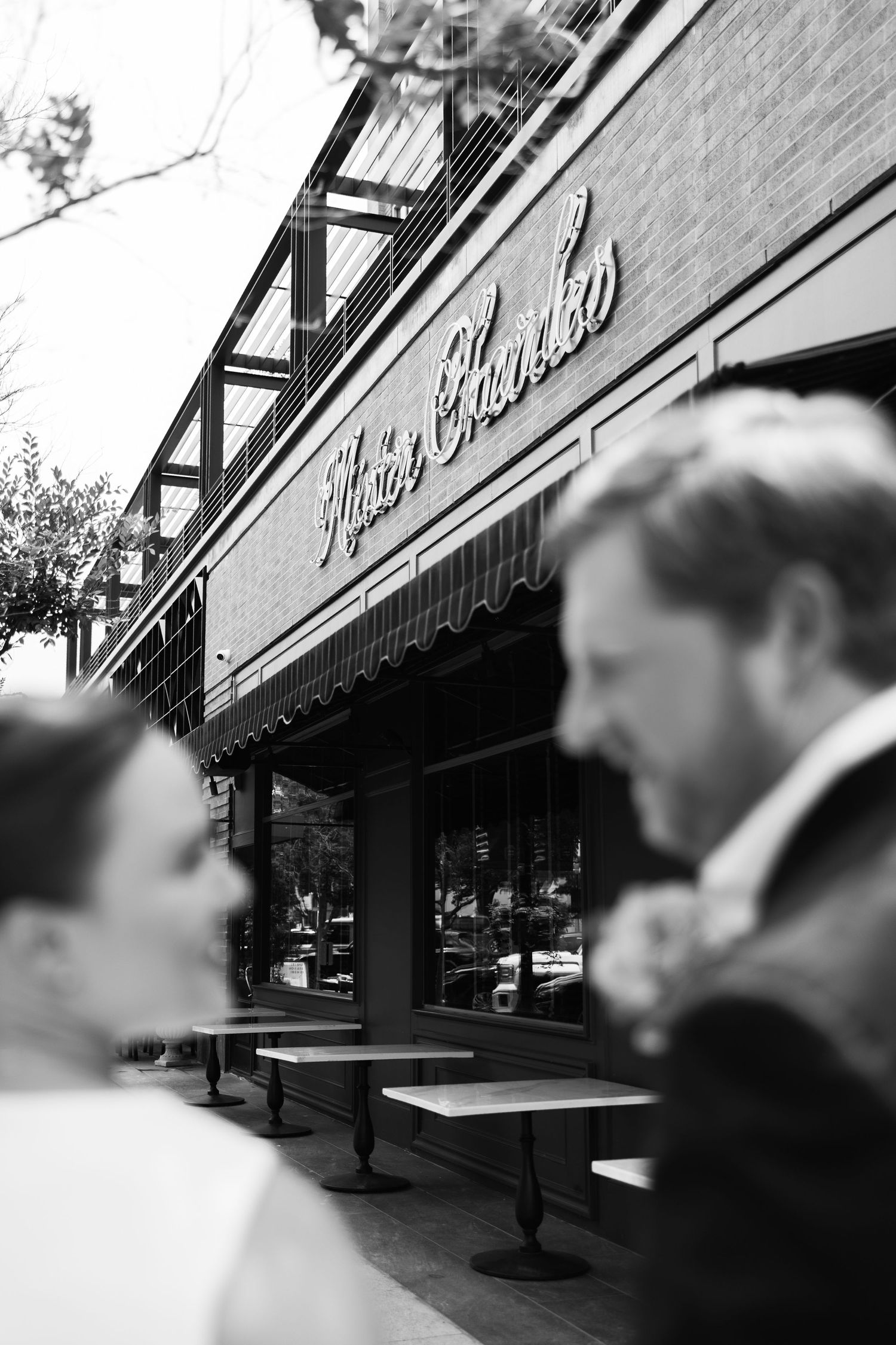 Black and white photo of a couple in formal attire standing outside Mario Guerrero restaurant with outdoor seating.