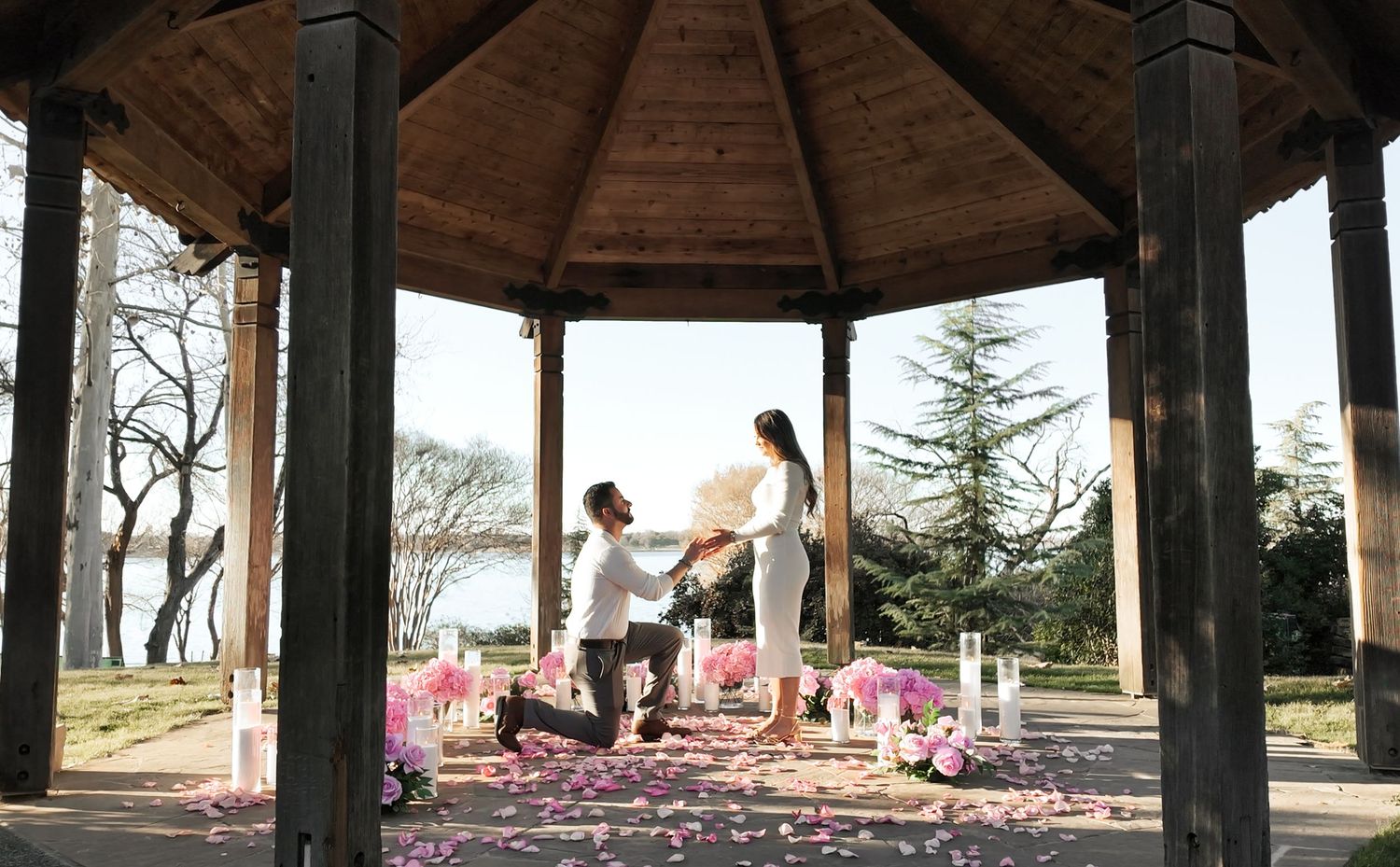 A panoramic view of a wooden gazebo structure with pink cherry blossom petals scattered on the ground.