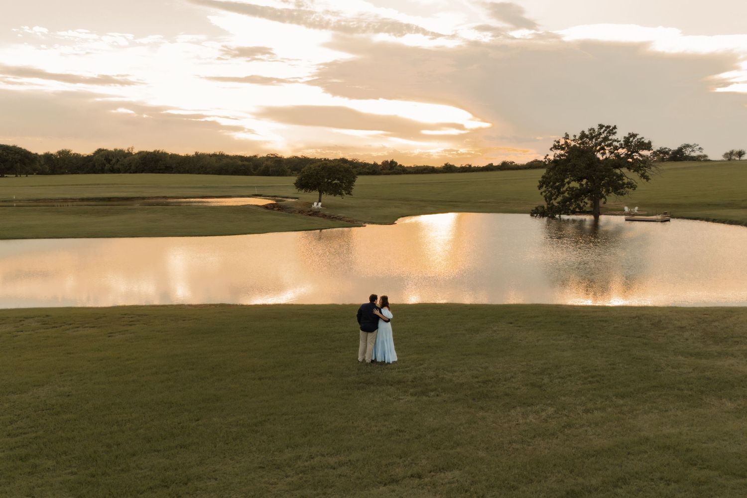 Bride and groom stand together at sunset by a serene pond on a lush green golf course.