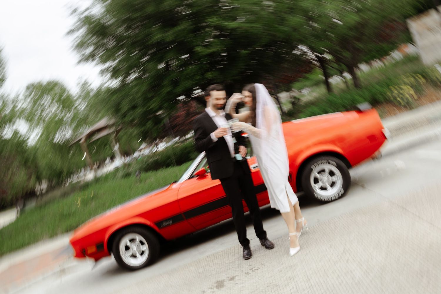 Bride and groom posing in front of a classic red sports car on their wedding day.
