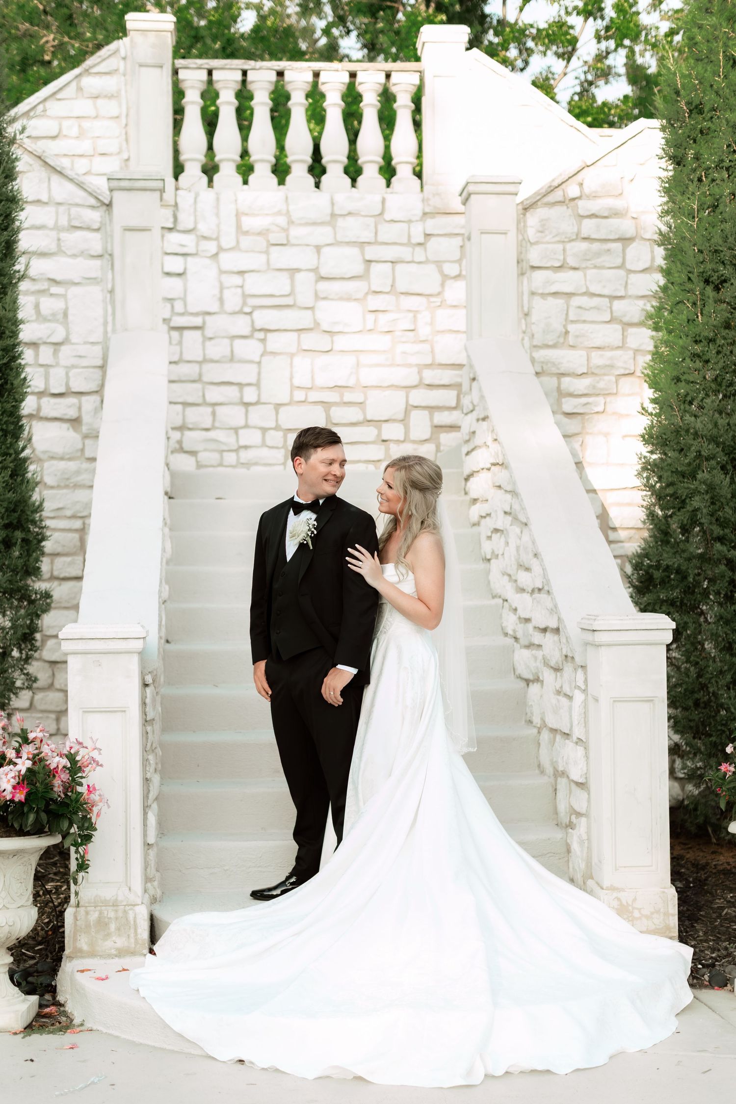 Elegant couple poses by white stone pillars and balustrade in formal wedding attire.