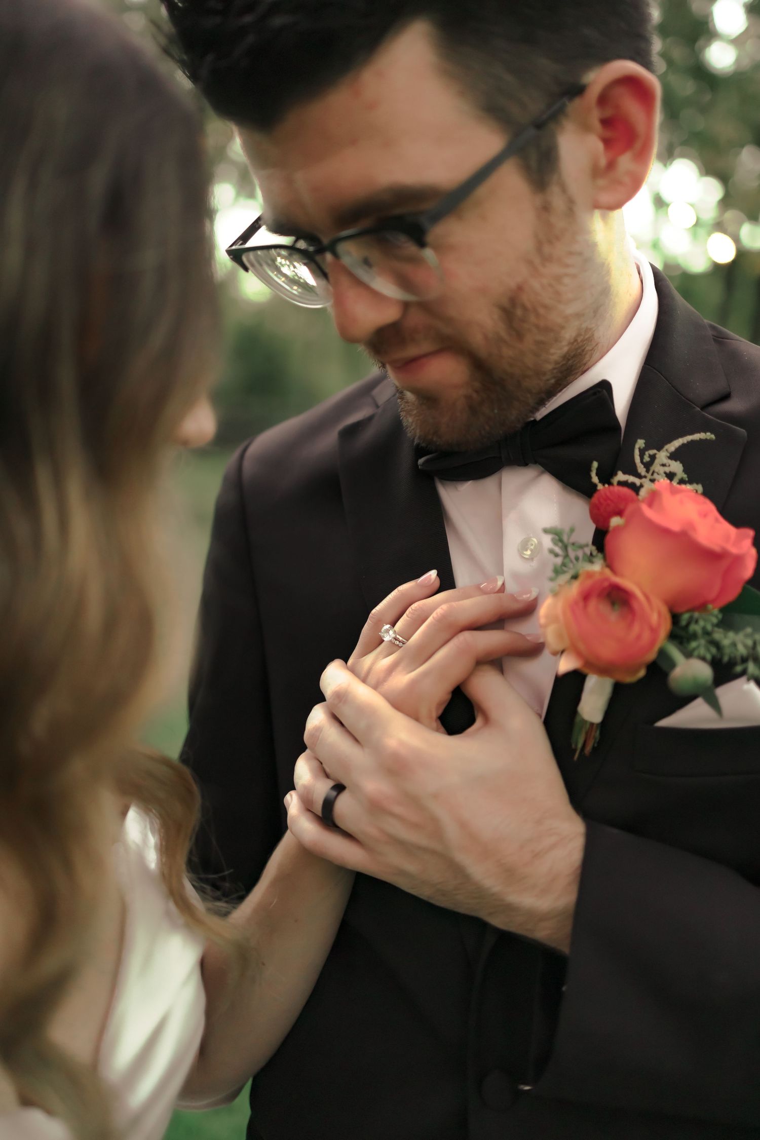 Close-up sequence of a groom in a black suit smelling a coral rose boutonniere pinned to his lapel.