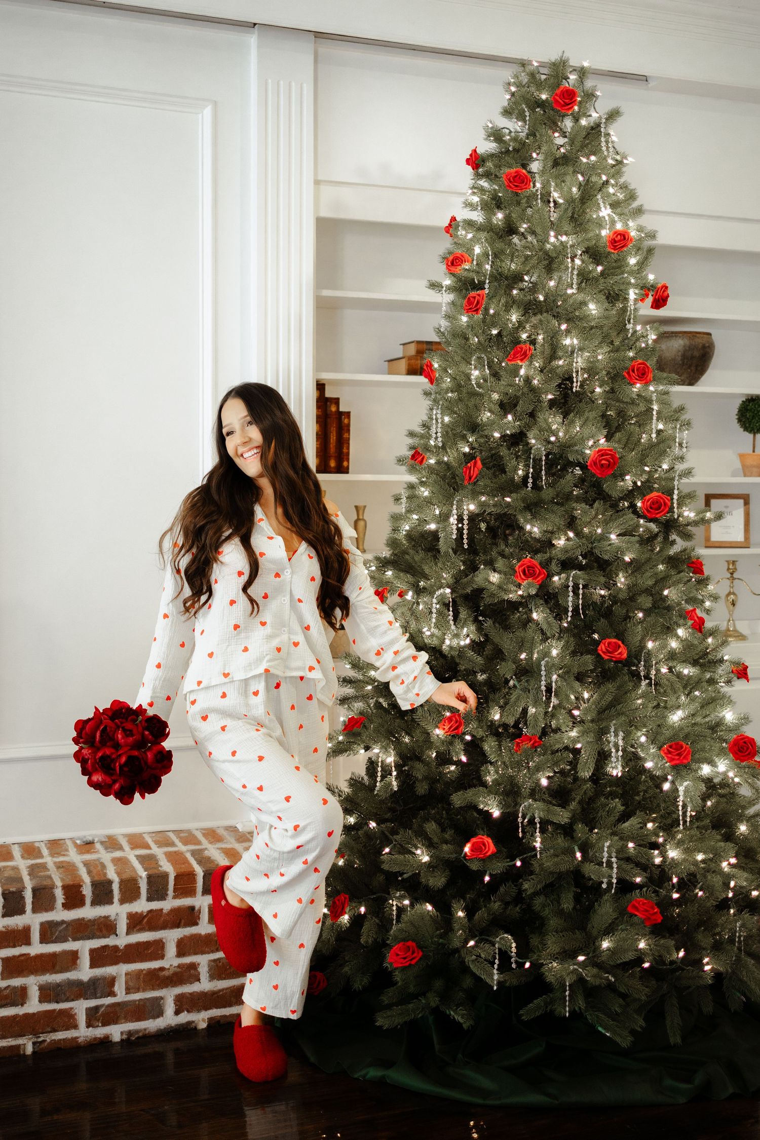 A festive Christmas scene with a decorated tree adorned with red ornaments and white lights against a white wall.