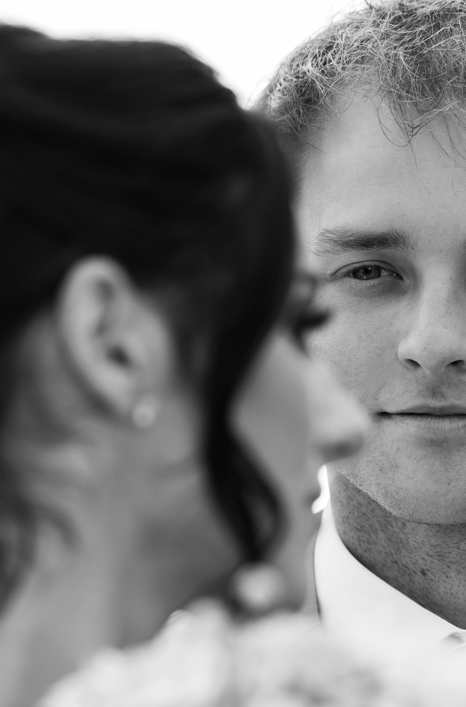 Black and white wedding photo of a groom smiling with bride in foreground, romantic close-up portrait.