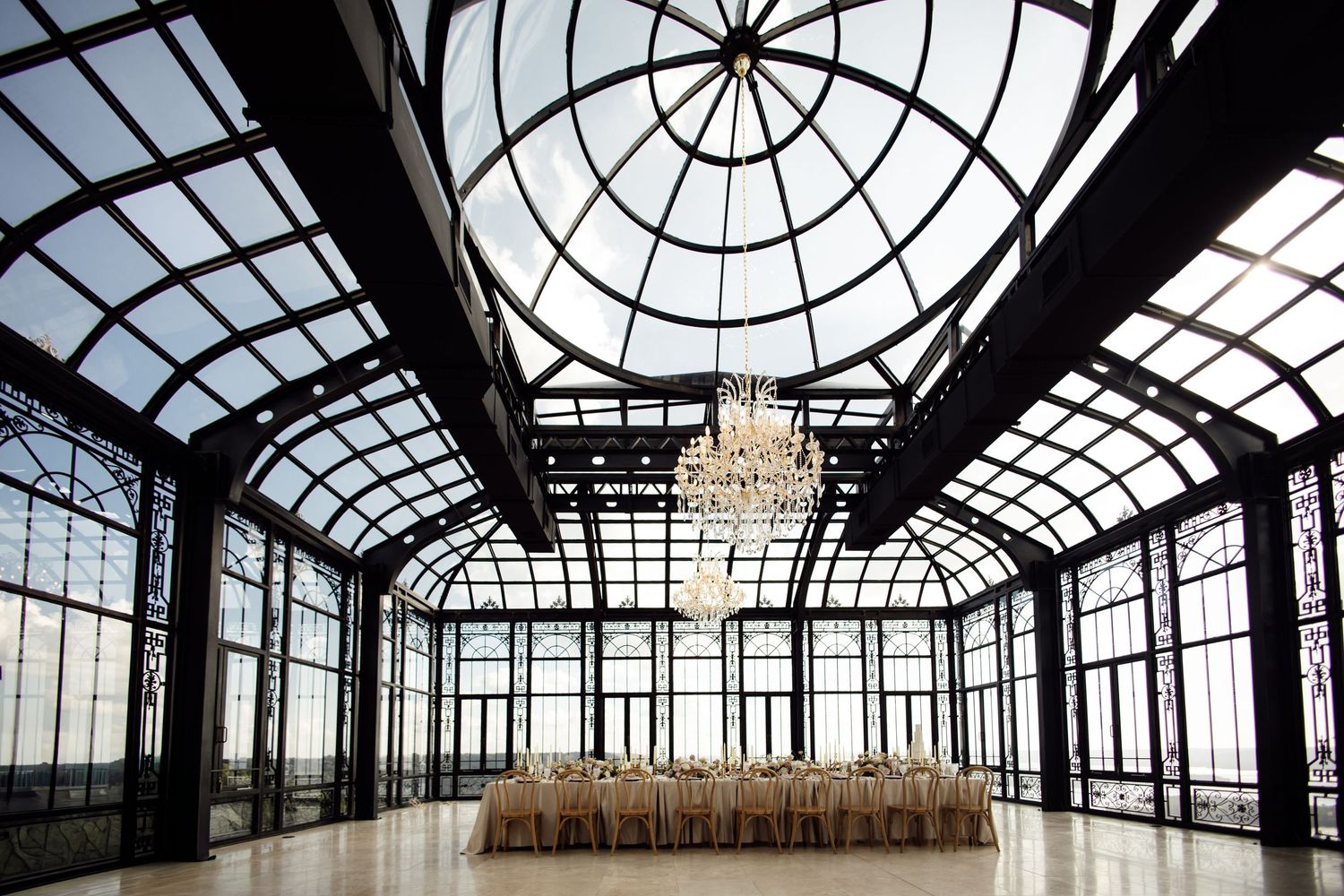 Elegant glass-domed event hall with chandelier and banquet tables set for a formal wedding reception.