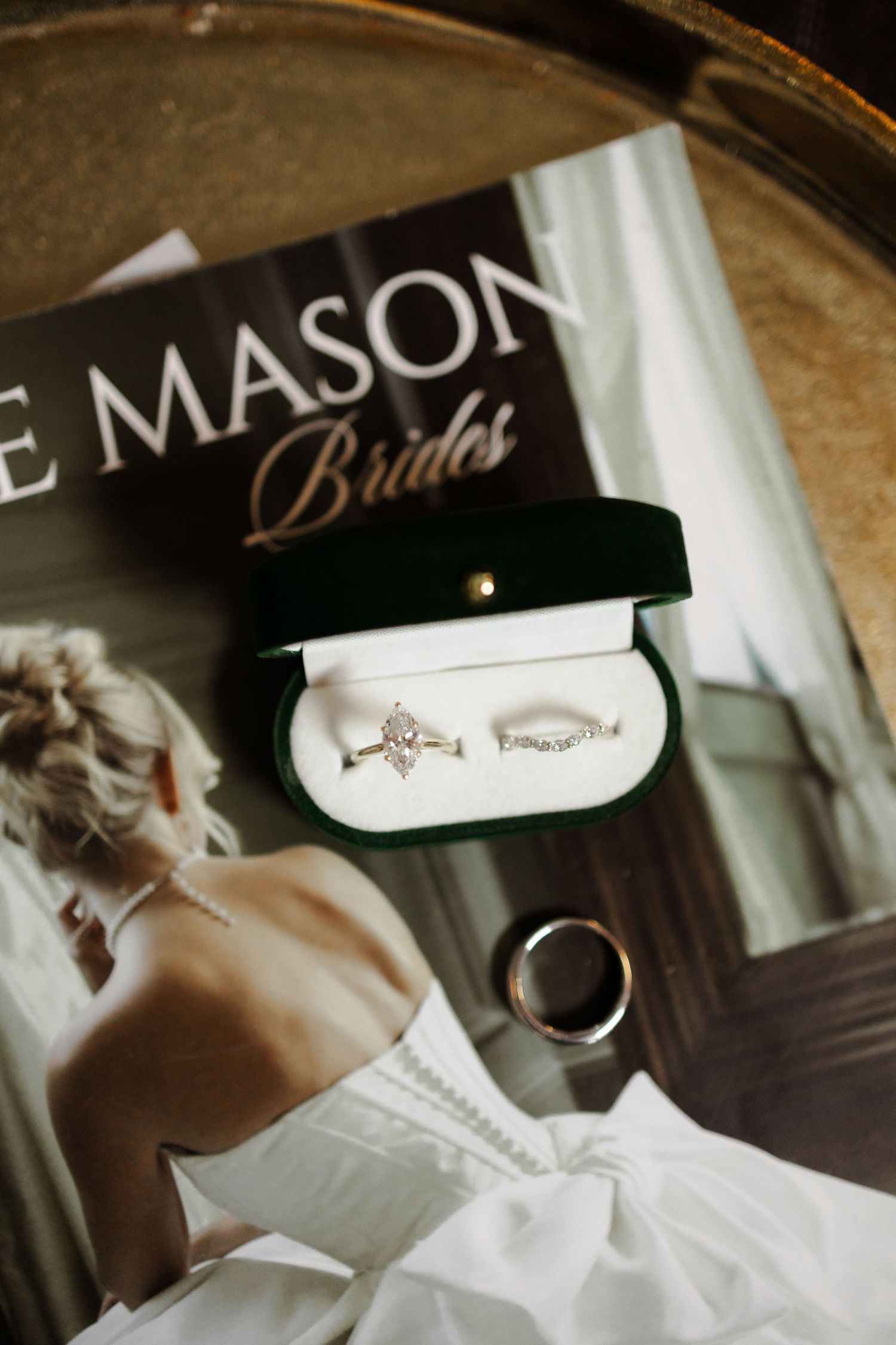 Green velvet ring box with diamond engagement ring and wedding band on bridal magazine beside groom ring.