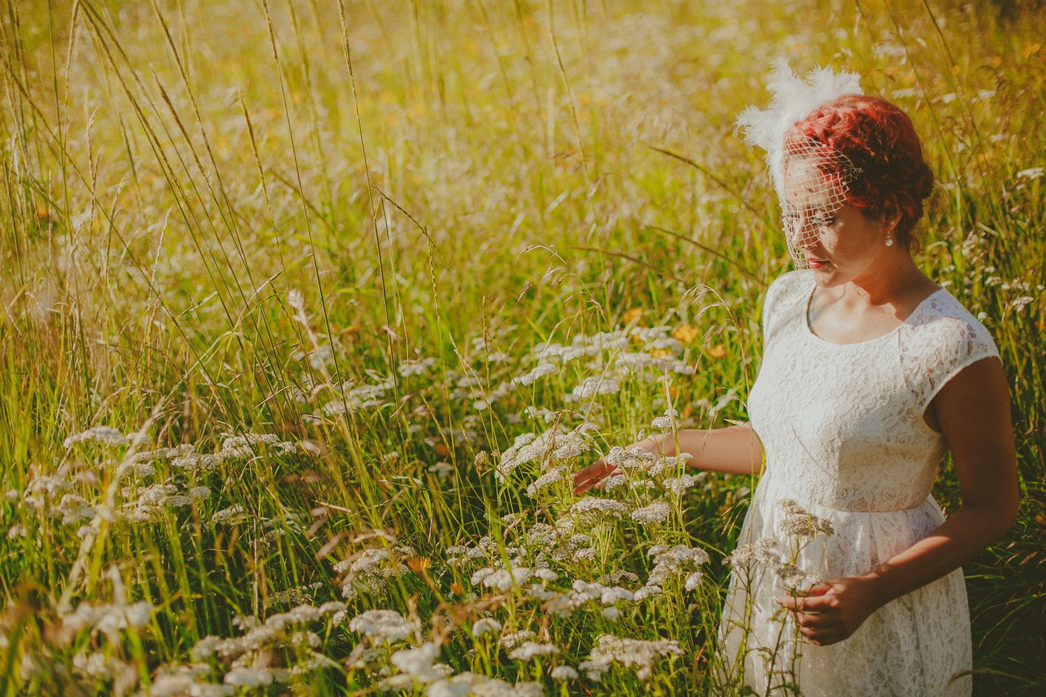 A woman with pink hair in a white lace dress walks through a golden wildflower meadow.
