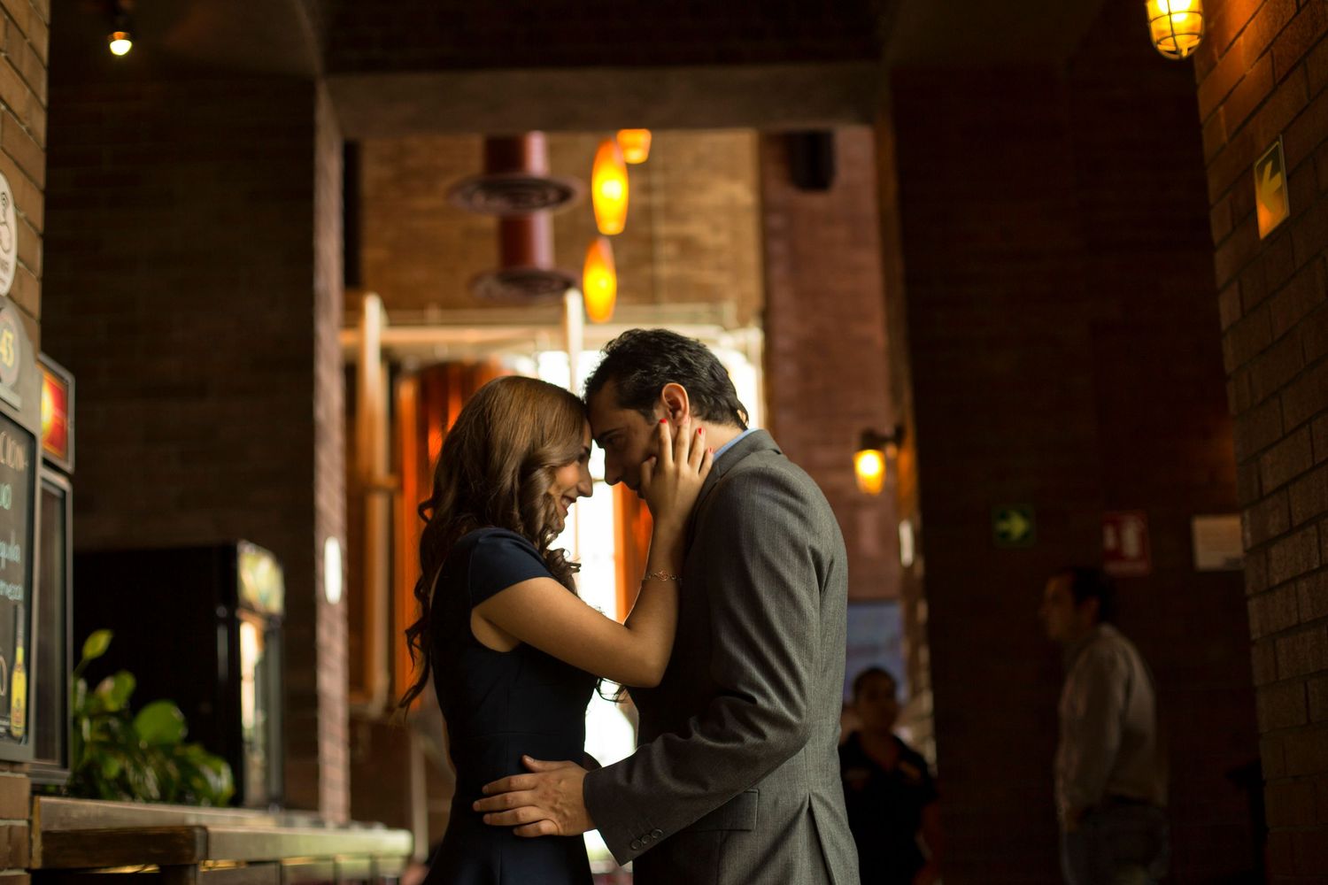Romantic couple sharing an intimate moment, nearly kissing in a warmly lit restaurant entrance at night.