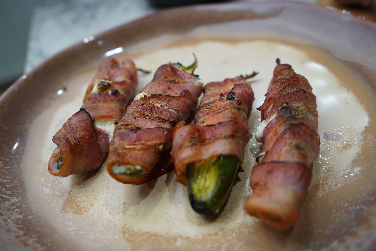 Bacon-wrapped jalapeno poppers served on a round plate, golden and crispy after being grilled to perfection.