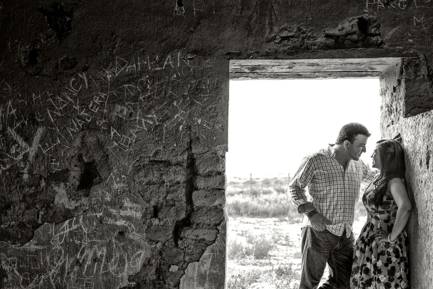 Black and white photo of a couple sharing a romantic moment in a rustic stone doorway with graffiti-covered walls.
