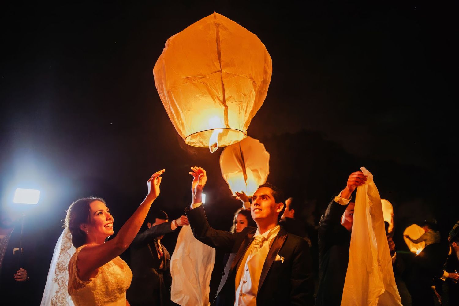 Bride and groom releasing glowing sky lantern at night during wedding celebration outdoors.