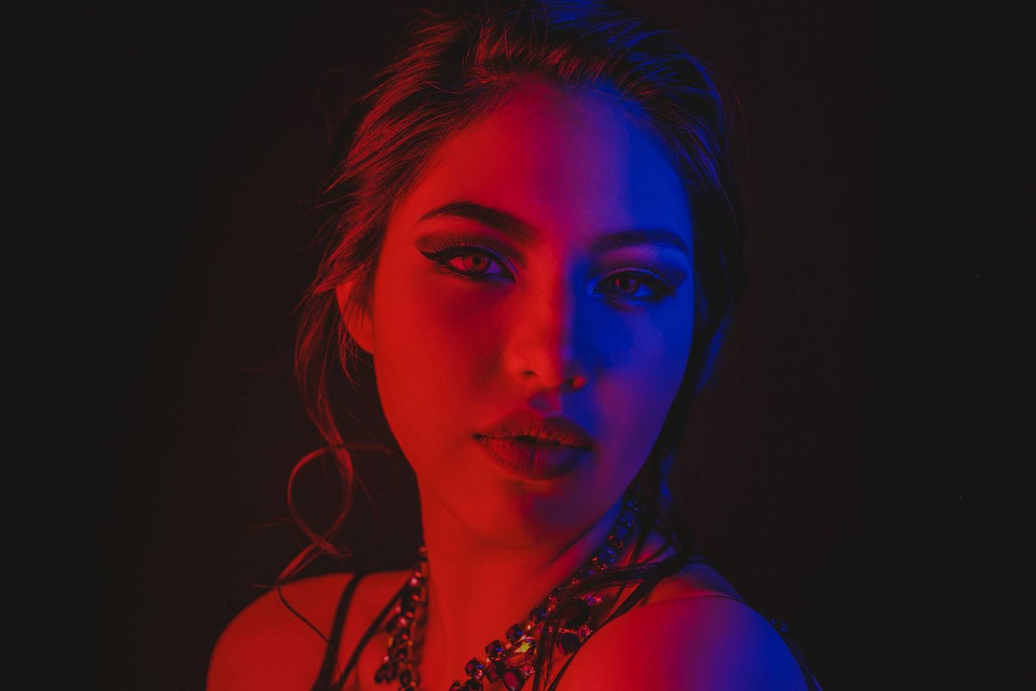 Young woman portrait with dramatic red and blue neon lighting against dark background.
