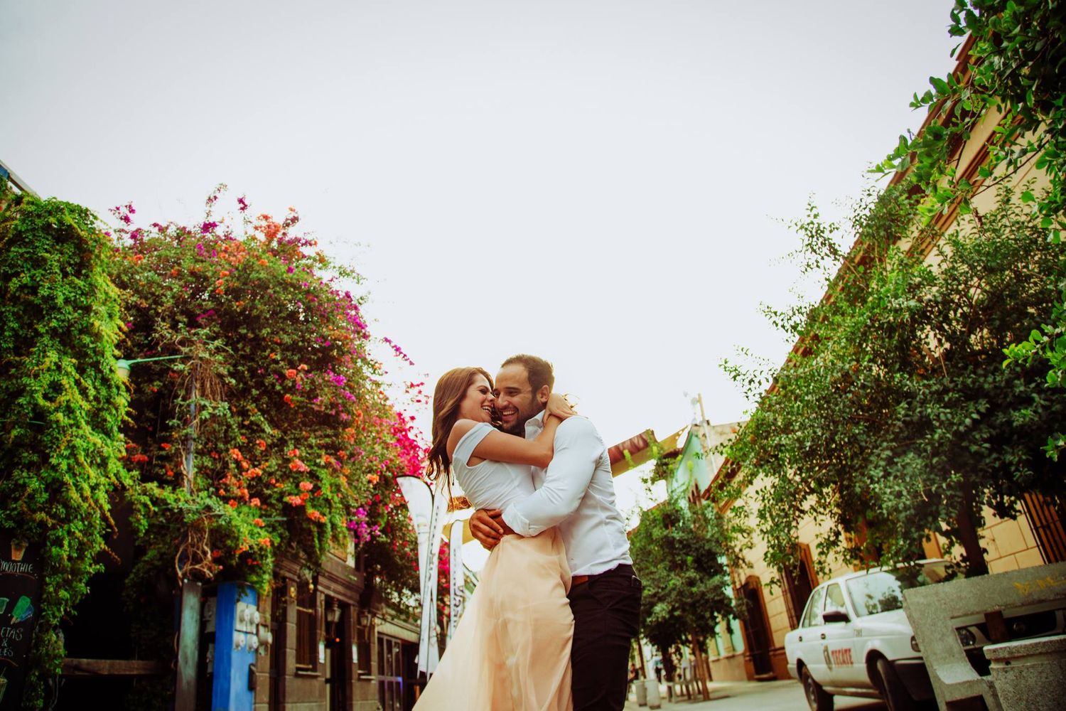 Couple embracing on a charming street lined with colorful bougainvillea and green ivy.