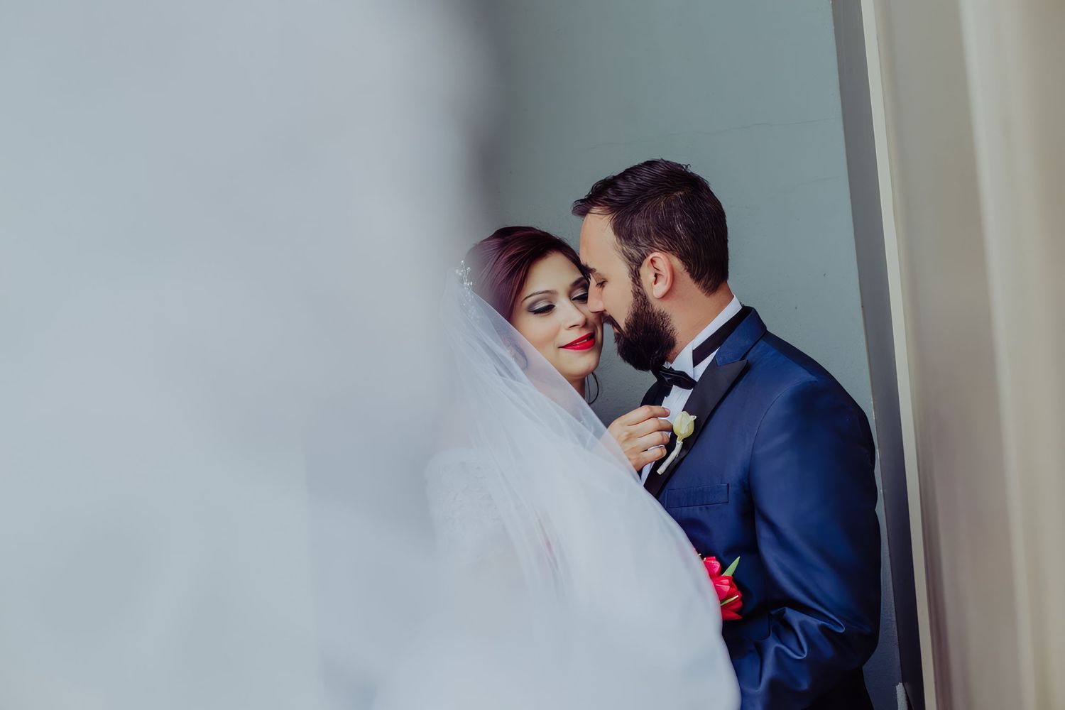 Romantic wedding couple sharing an intimate moment, bride in white veil and groom in blue suit with bow tie.