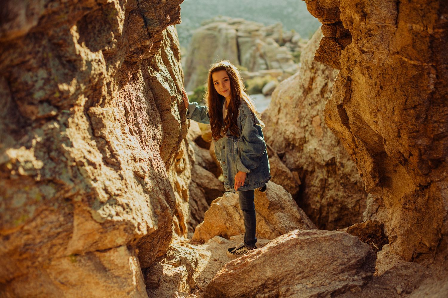 A young woman in a blue dress and boots navigates rocky terrain in a sunlit canyon.