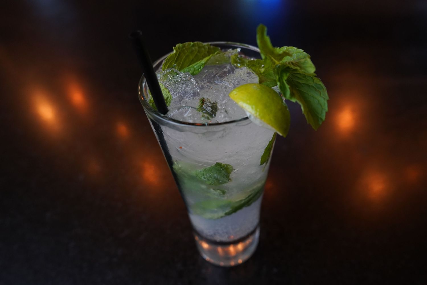 Fresh mojito cocktail with mint leaves, lime, and ice in a tall glass on a dark surface.