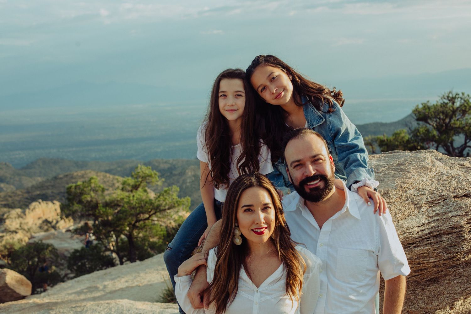 Family of four posing on a rocky mountain overlook with scenic valley views and blue sky backdrop.
