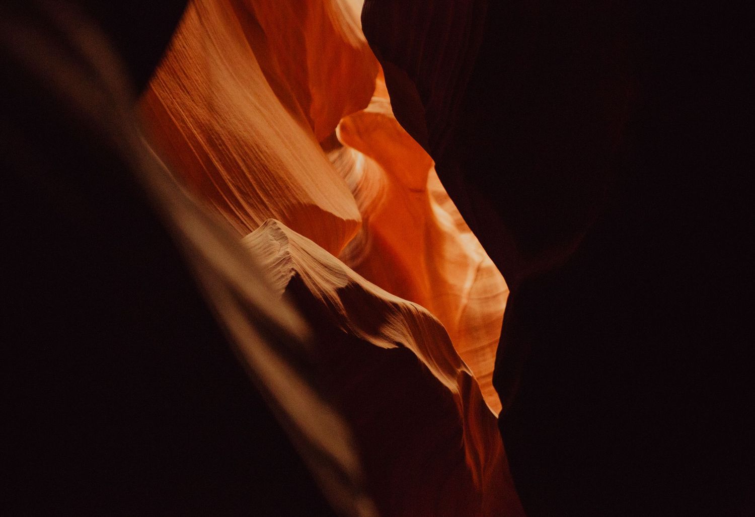 Glowing orange and red sandstone walls of Antelope Canyon slot canyon with dramatic light and shadow.