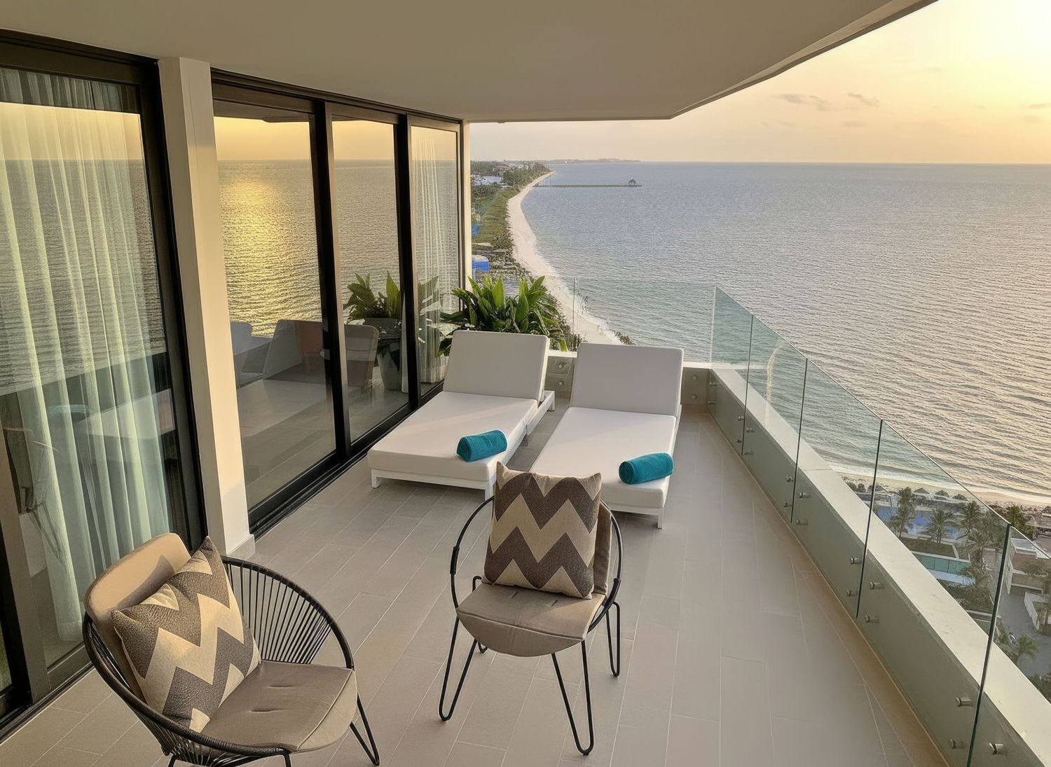 Luxury balcony with lounge chairs overlooking a stunning ocean sunset view and pristine beach at a modern resort.