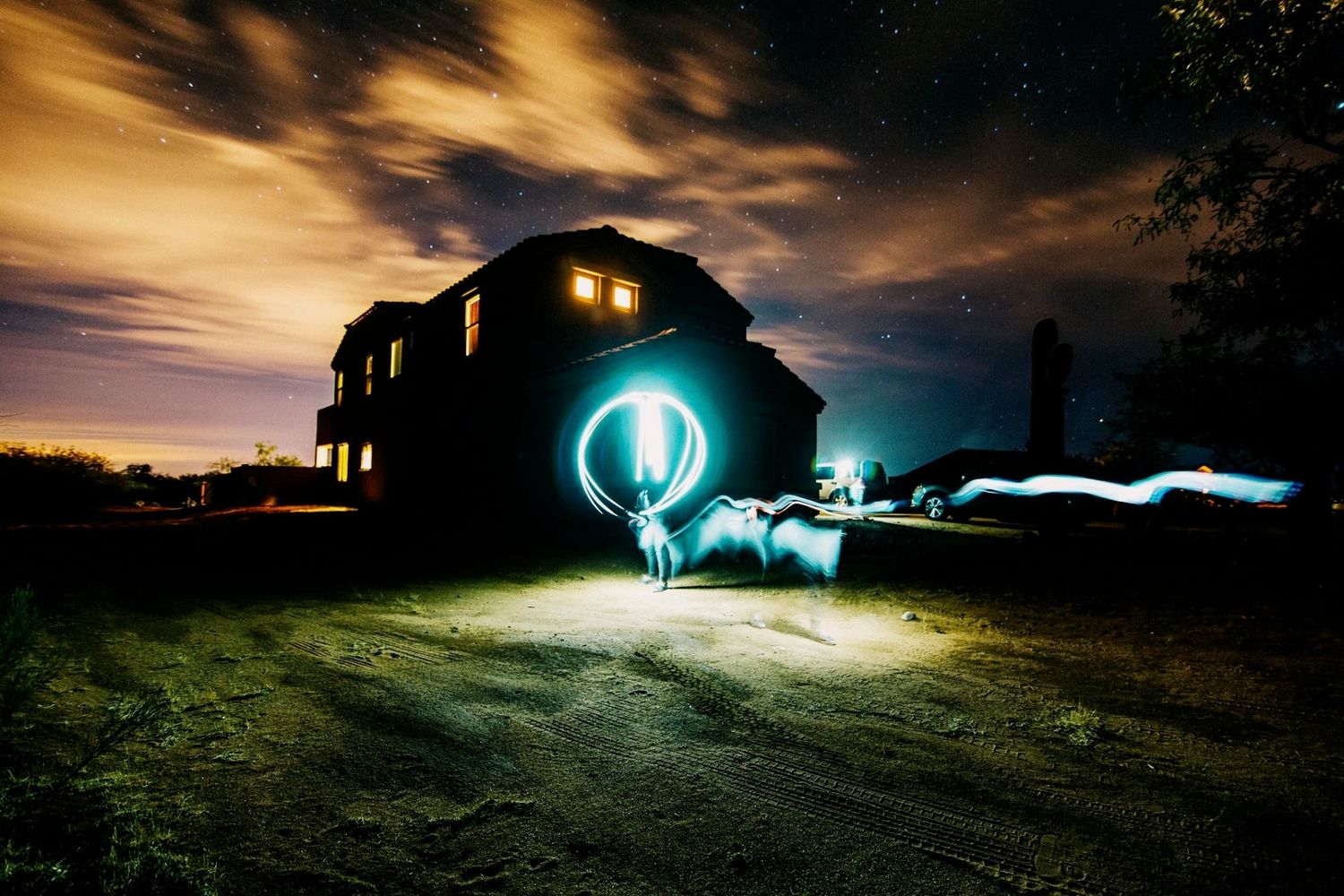 Light painting photography at night outside a dark house with glowing orb and streaks of light under a cloudy sky.