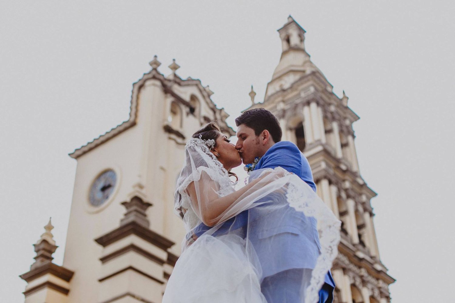 Bride and groom share a romantic kiss in front of a historic church on their wedding day.
