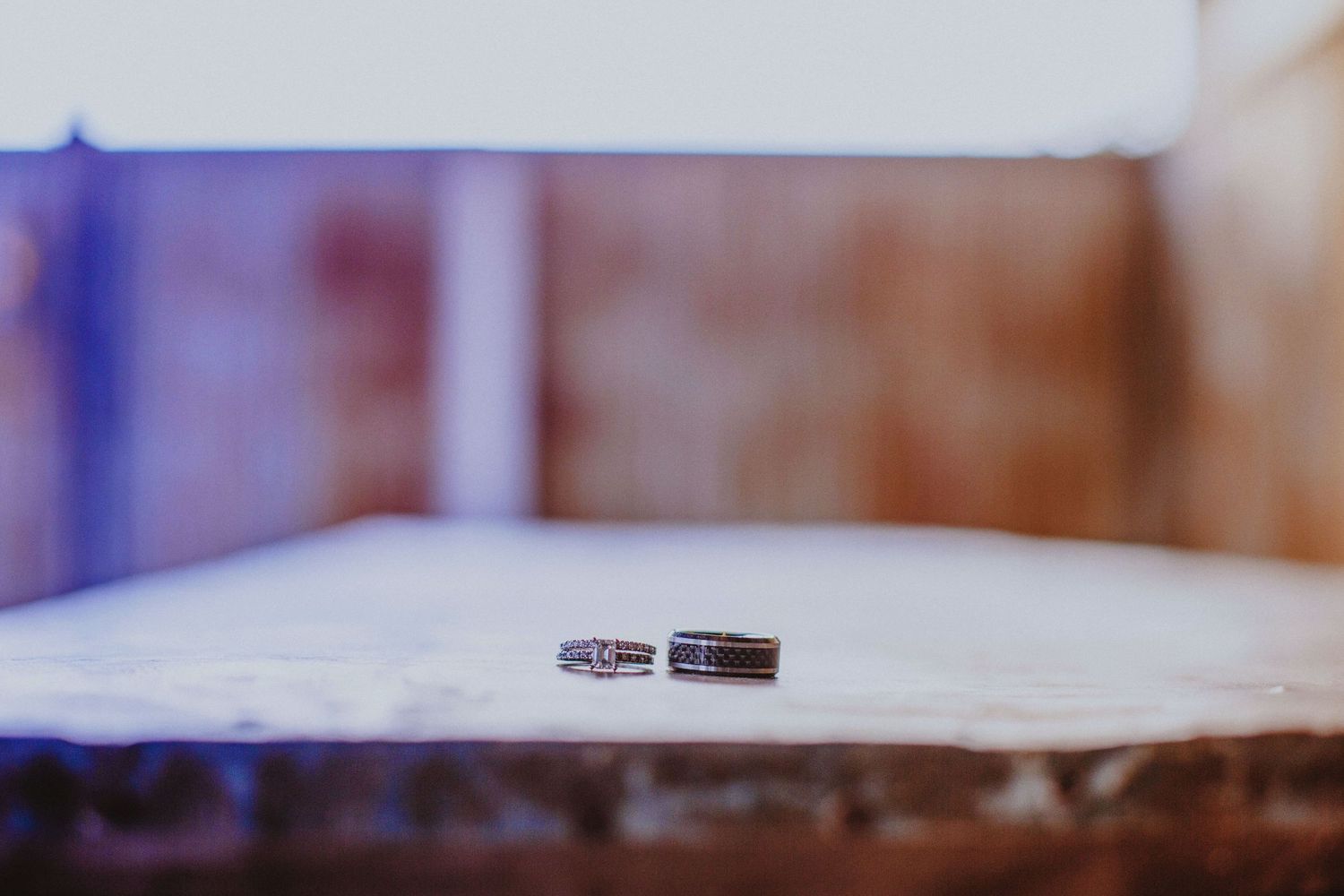 Two elegant wedding bands resting on a white surface with a softly blurred bokeh background.