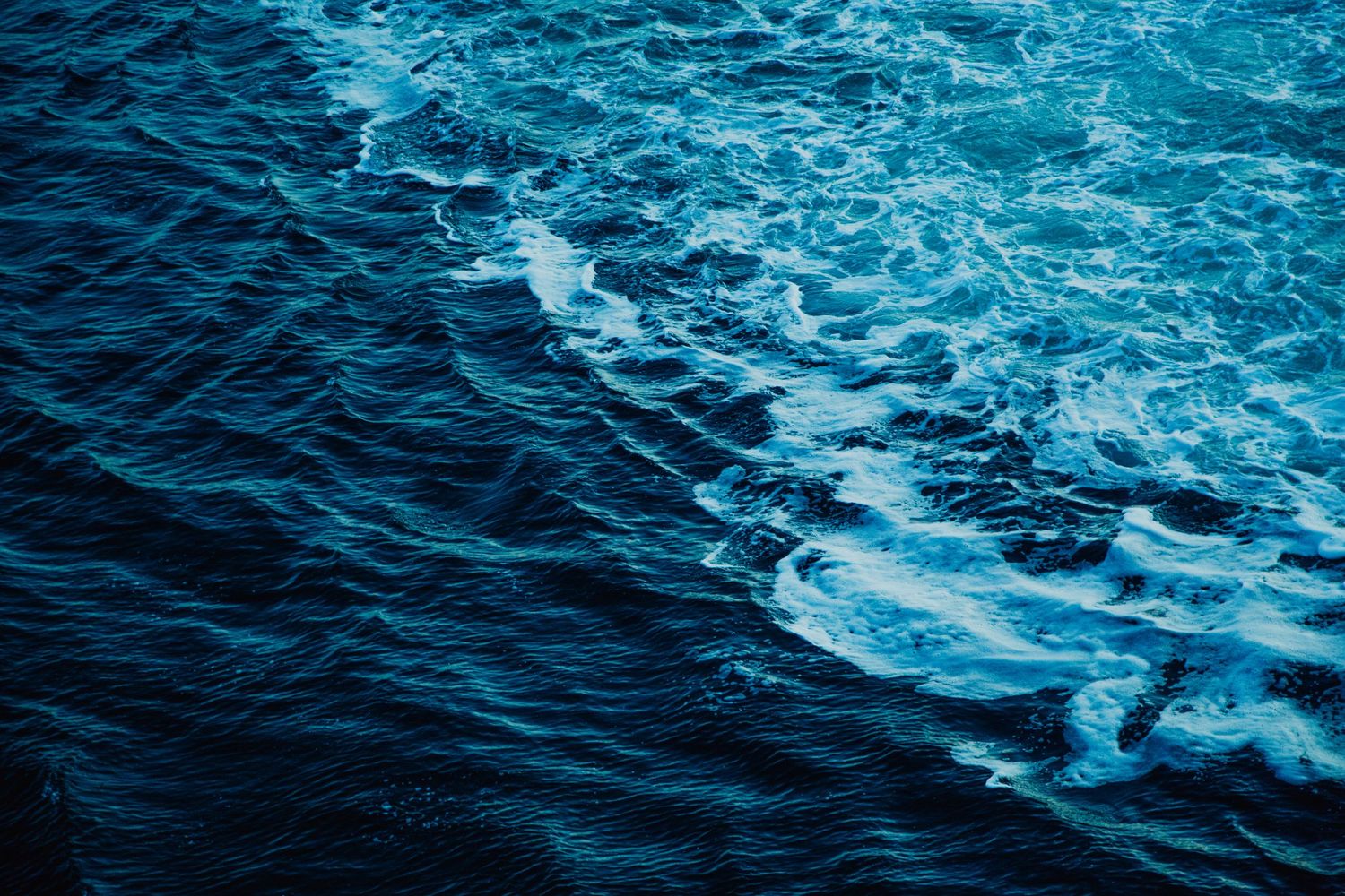 Deep blue ocean waves with white foam swirling on the surface, capturing the raw beauty of the open sea.
