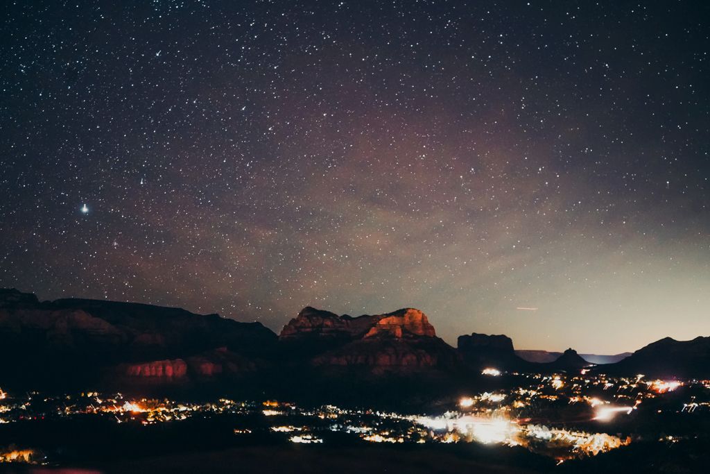 Stunning night sky filled with stars over illuminated mountain town with glowing red rock formations.