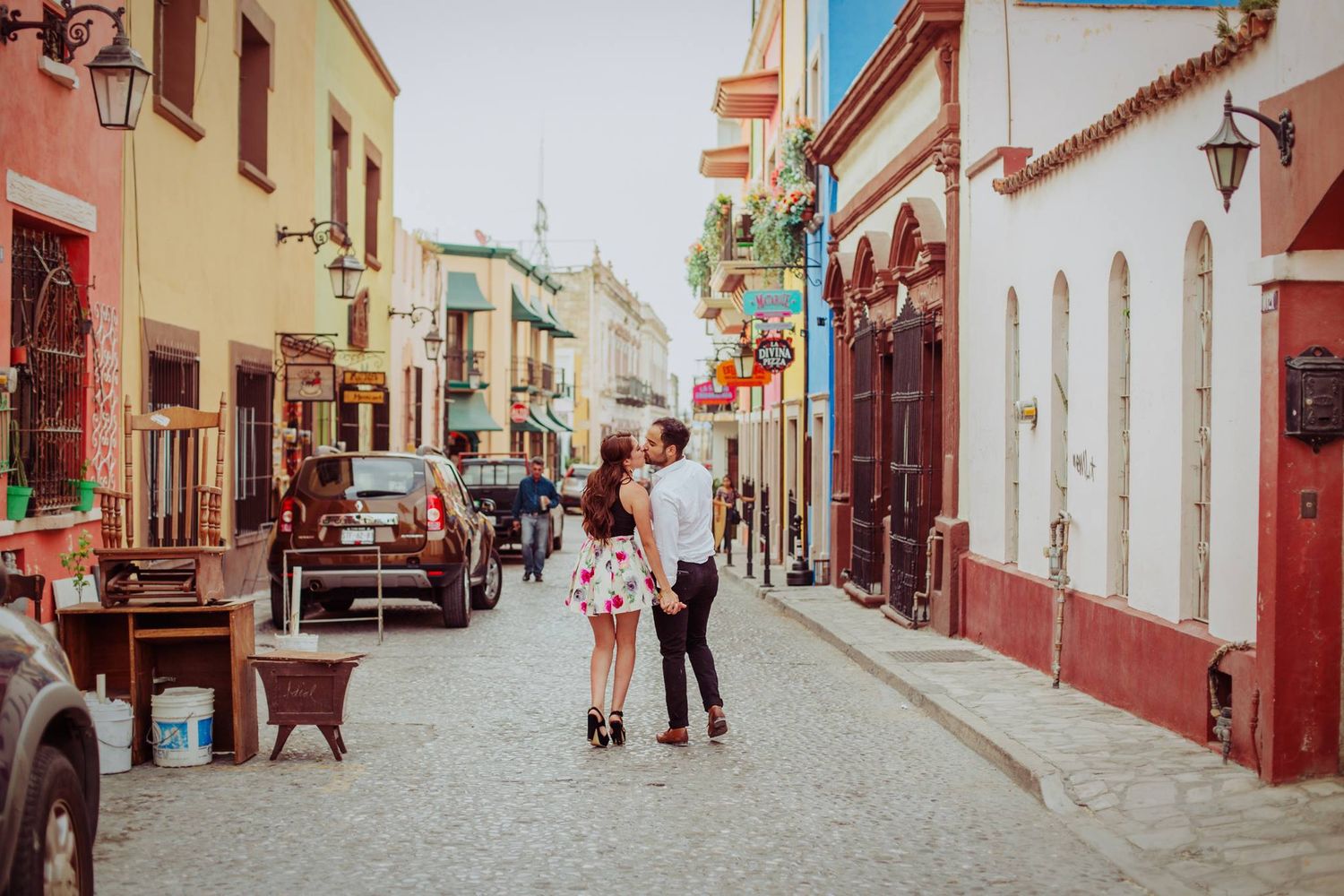 Romantic couple kissing on a colorful cobblestone street in a charming Latin American town.